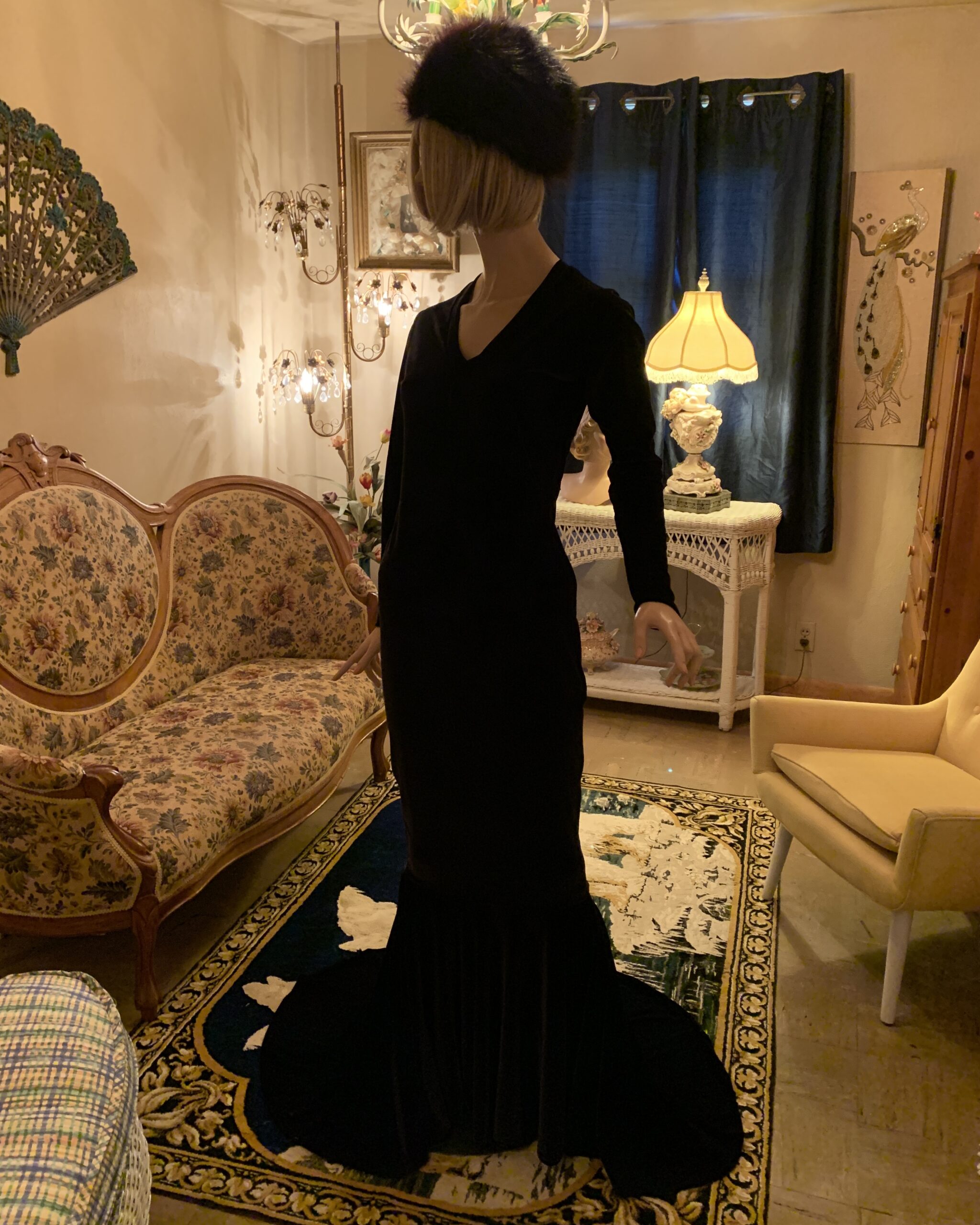 1990s black velvet evening gown with long sleeves and dramatic flared train displayed on a mannequin in a vintage salon.