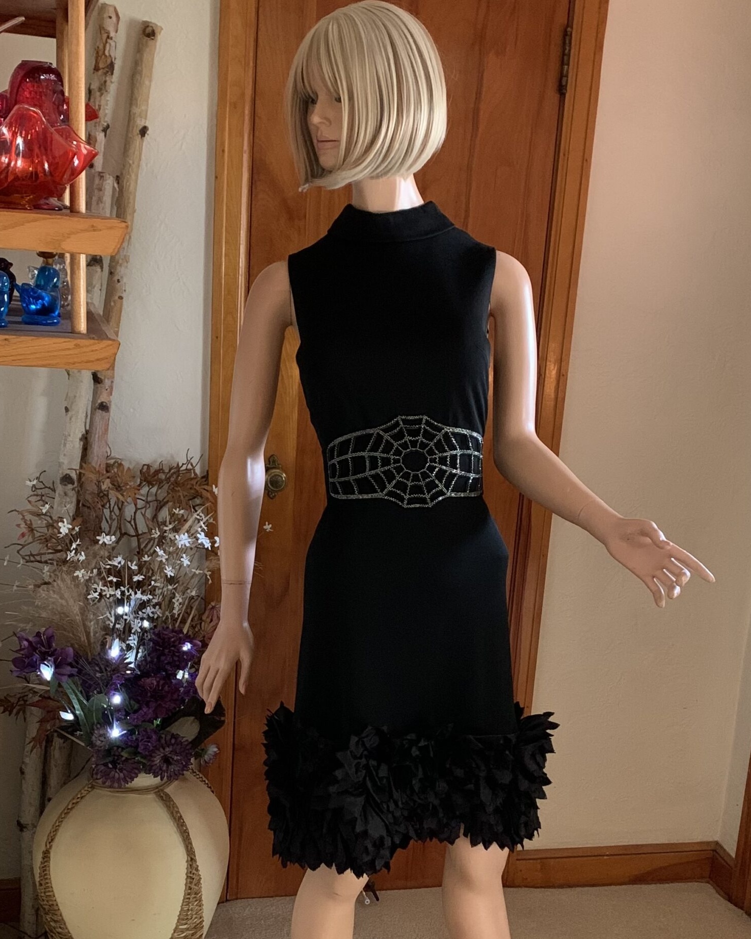 Black sleeveless mod dress displayed on mannequin with dimensional floral hem trim.