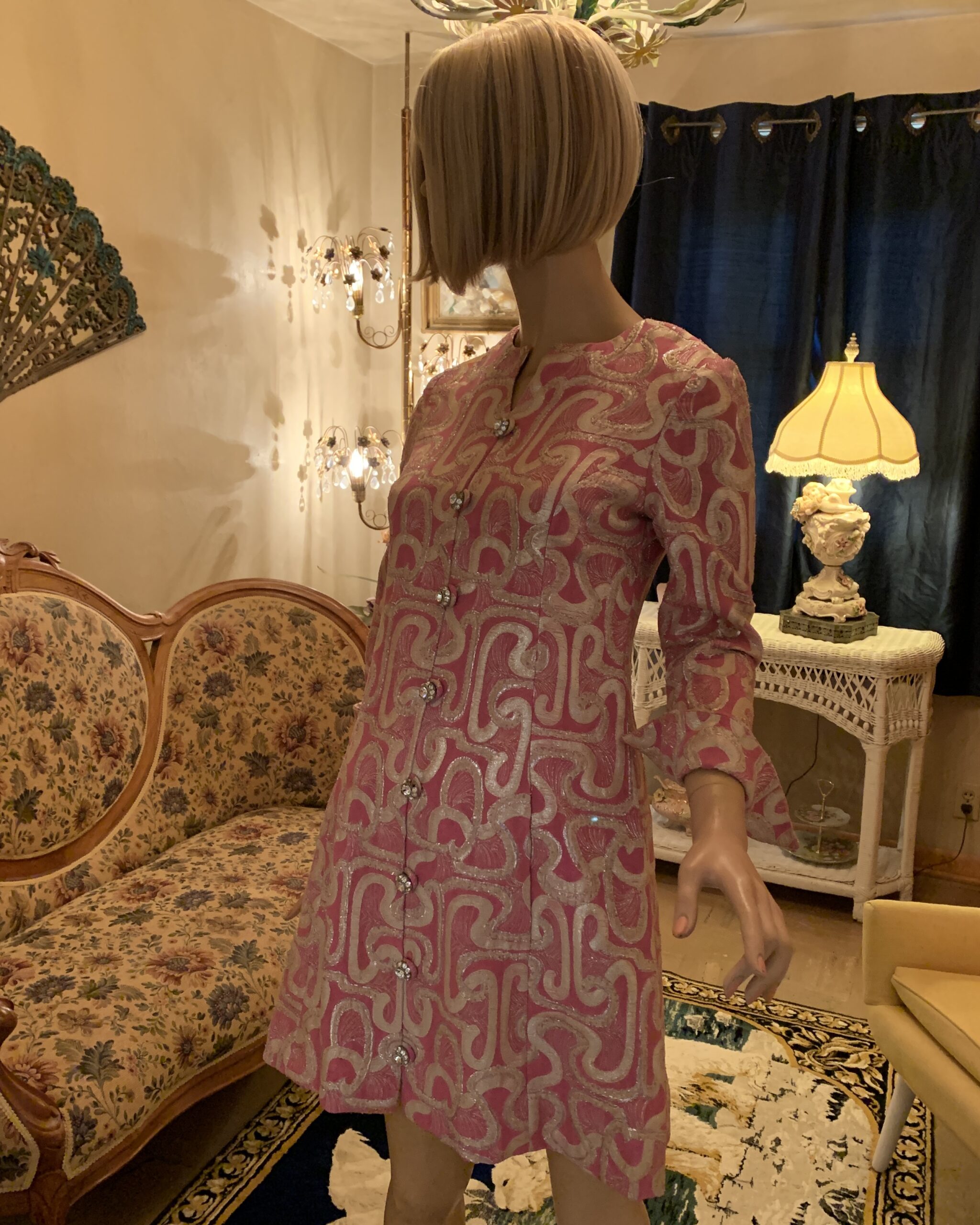 Side view of a vintage Oscar de la Renta pink metallic brocade coat dress featuring a shimmering swirl pattern and jeweled button front.