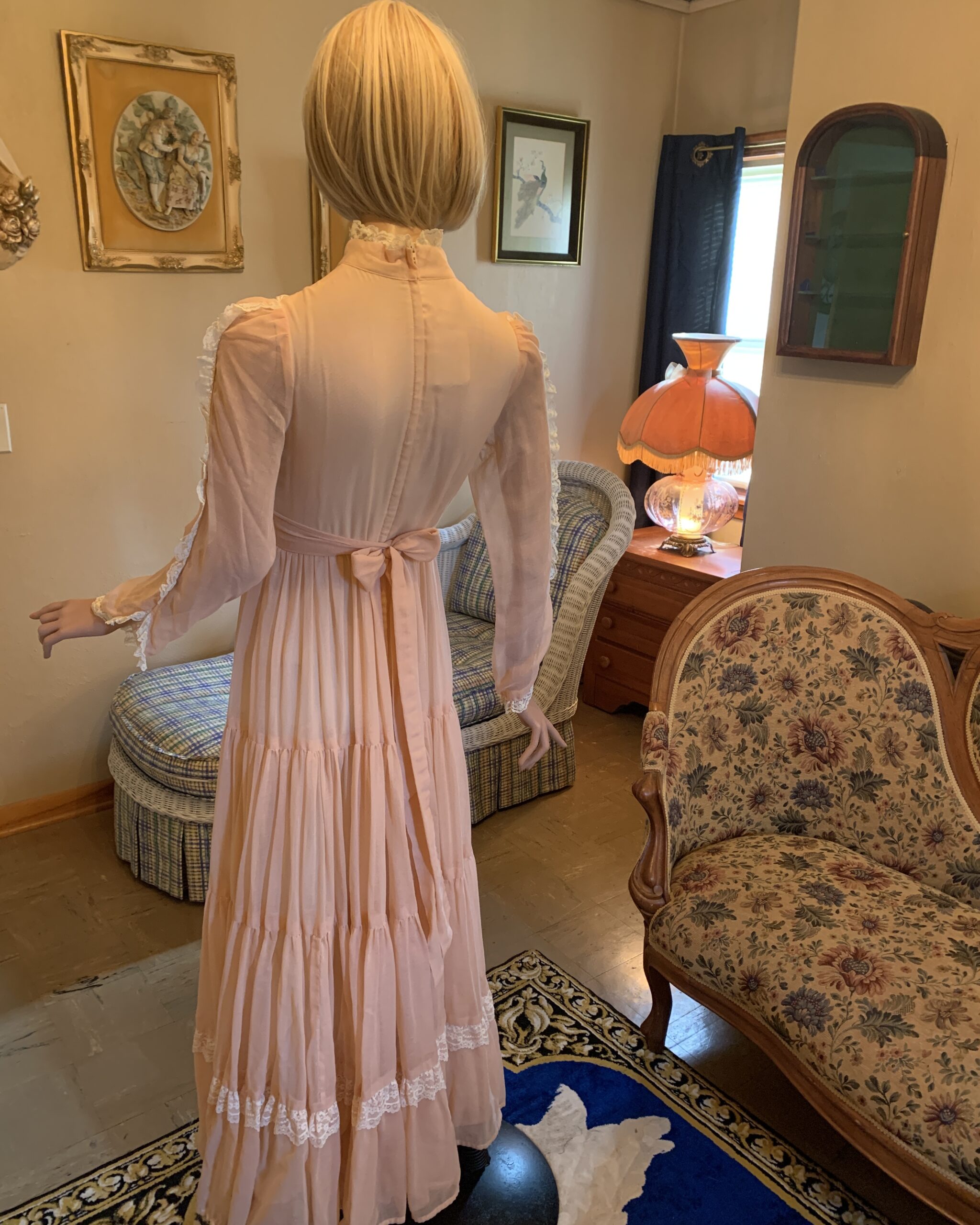 Back view of a vintage Gunne Sax peach prairie dress featuring a waist sash, sheer sleeves, and a full-length romantic silhouette.