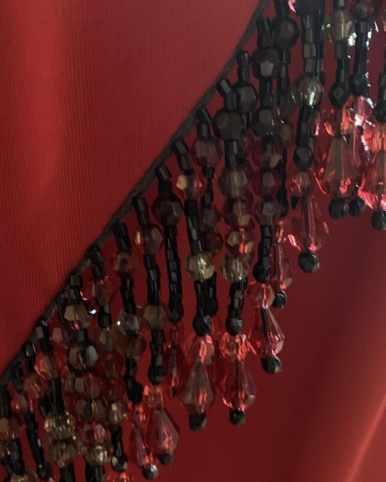 Close-up detail of faceted red bead fringe and asymmetrical overlay on vintage Jack Bryan evening gown.