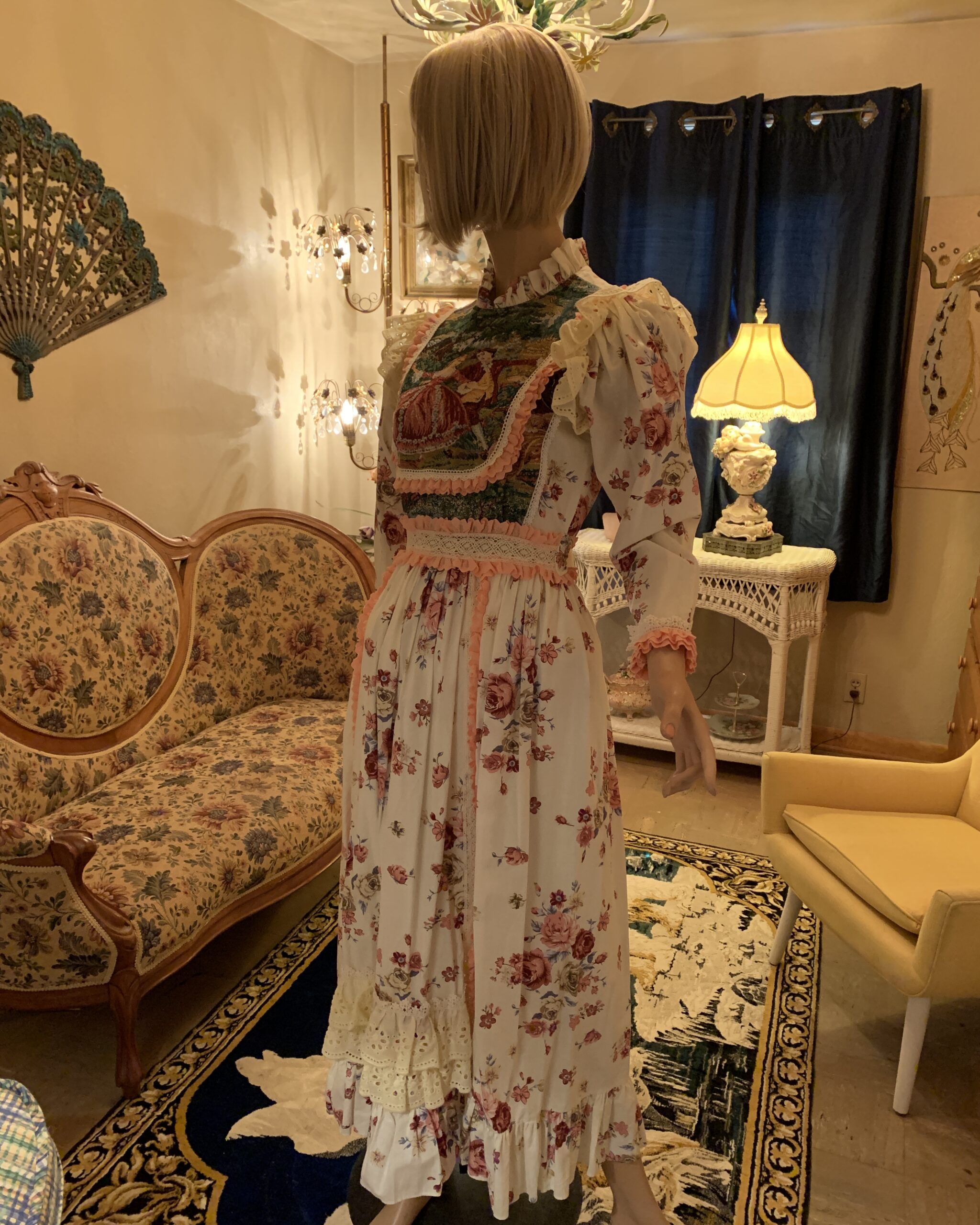 Side view of a vintage floral prairie dress featuring a woven tapestry bib, lace trim, ruffled shoulders, and a flowing floral skirt.