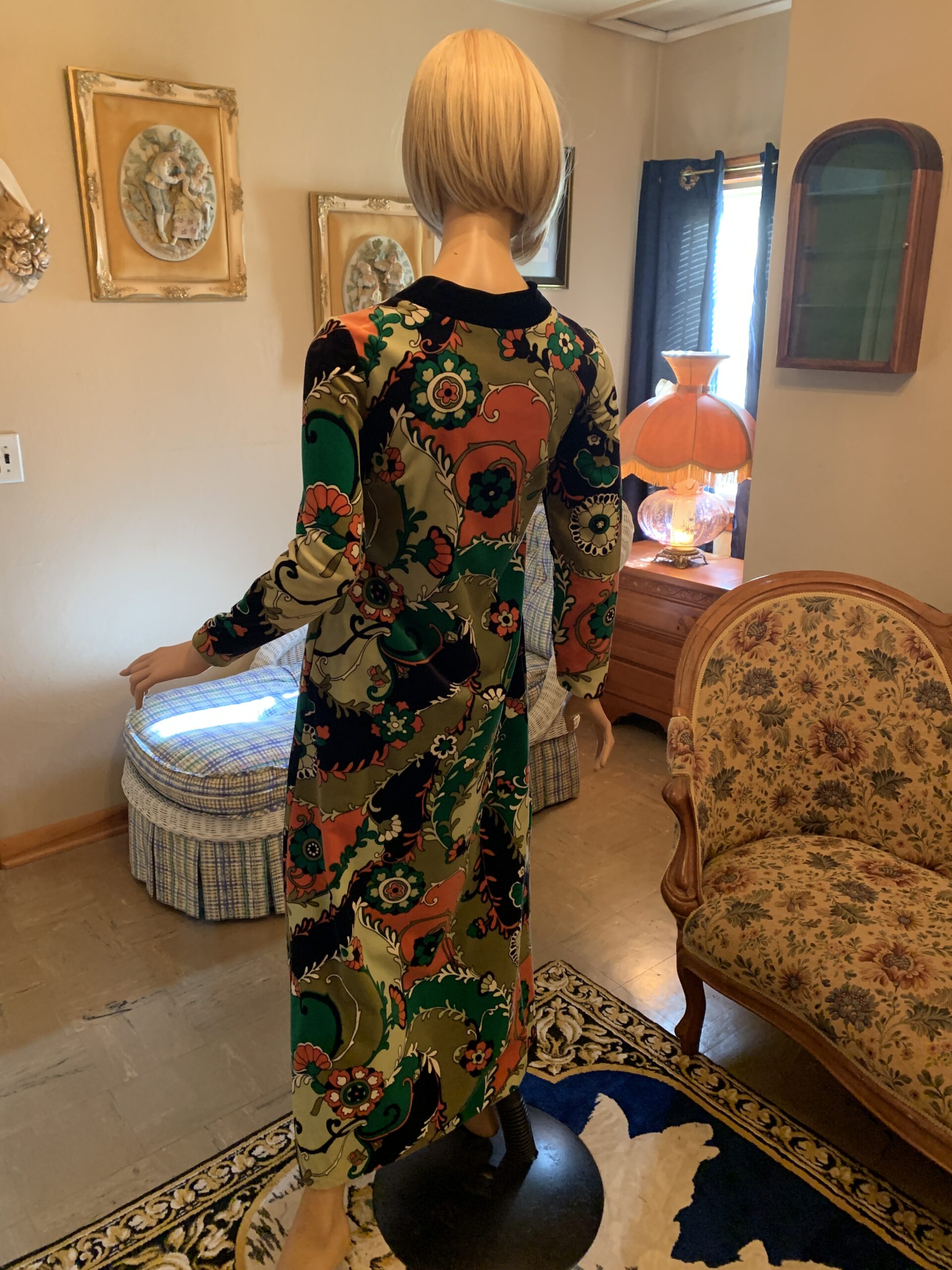 Back view of a vintage Bards Toronto floral print maxi dress showing the fitted bodice, long sleeves, and full-length skirt in an olive green, coral, and black floral pattern.