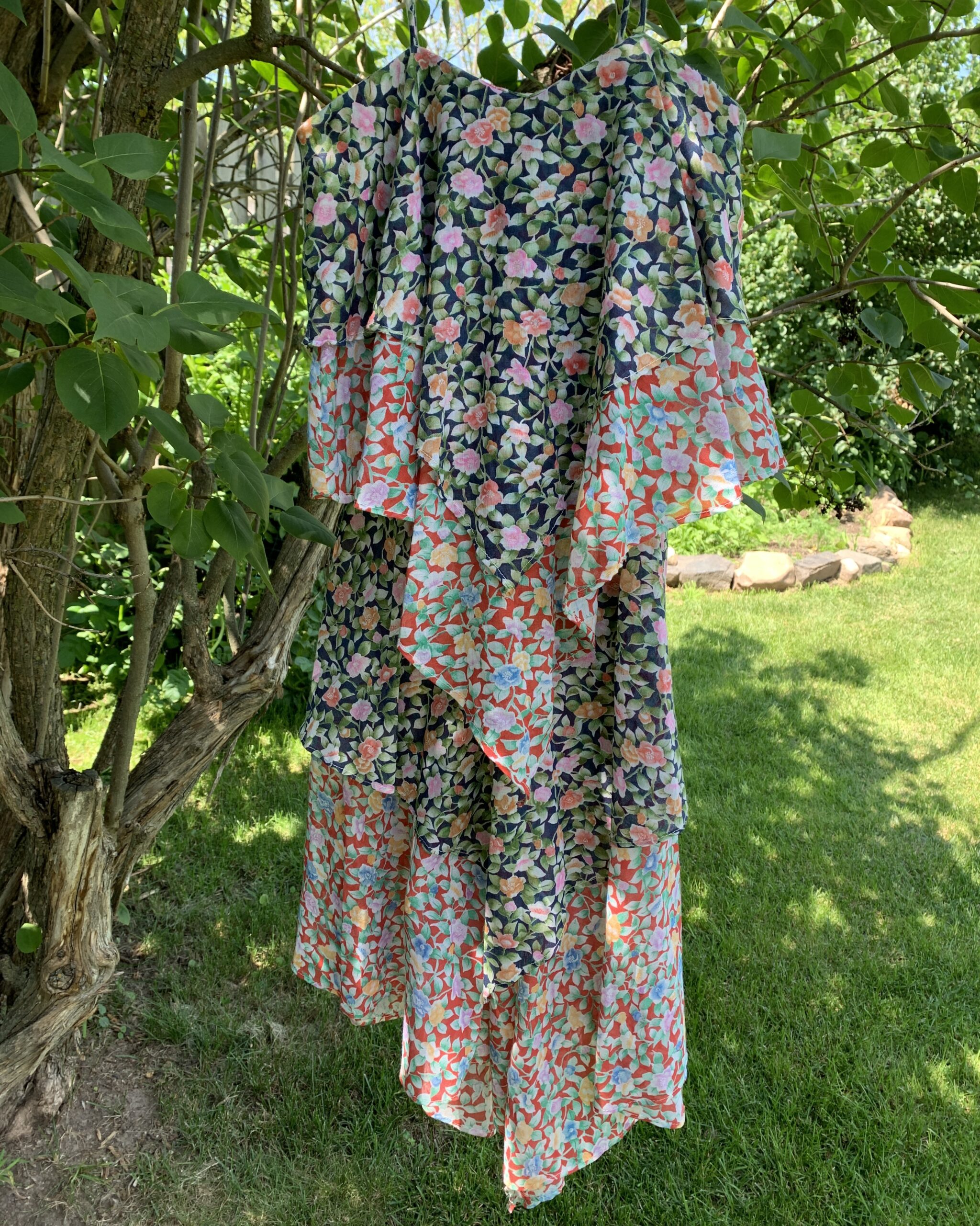 Vintage 1970s deadstock floral patchwork kerchief dress with spaghetti straps and layered asymmetrical handkerchief panels photographed hanging in a garden tree.