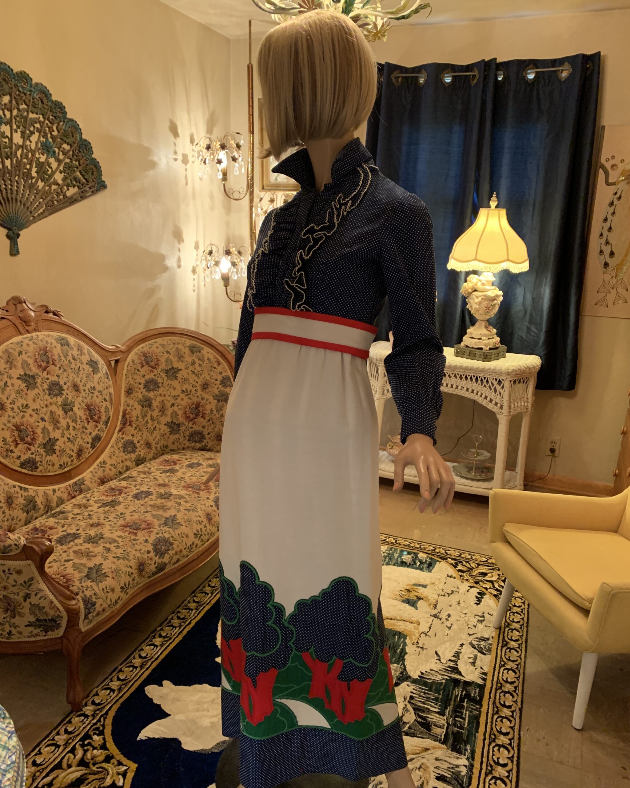 Side view of a vintage Eleanor Brenner Couture navy and white polka dot maxi dress featuring a ruffled bodice, empire waist, and colorful scenic appliqué landscape along the hem.