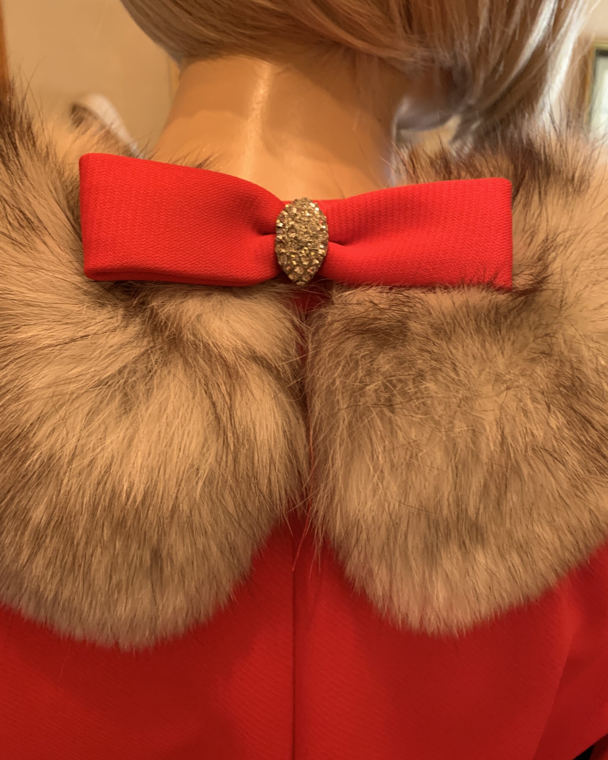 Close-up of decorative red bow with rhinestone center at the back collar of a 1960s Lilli Ann coat.