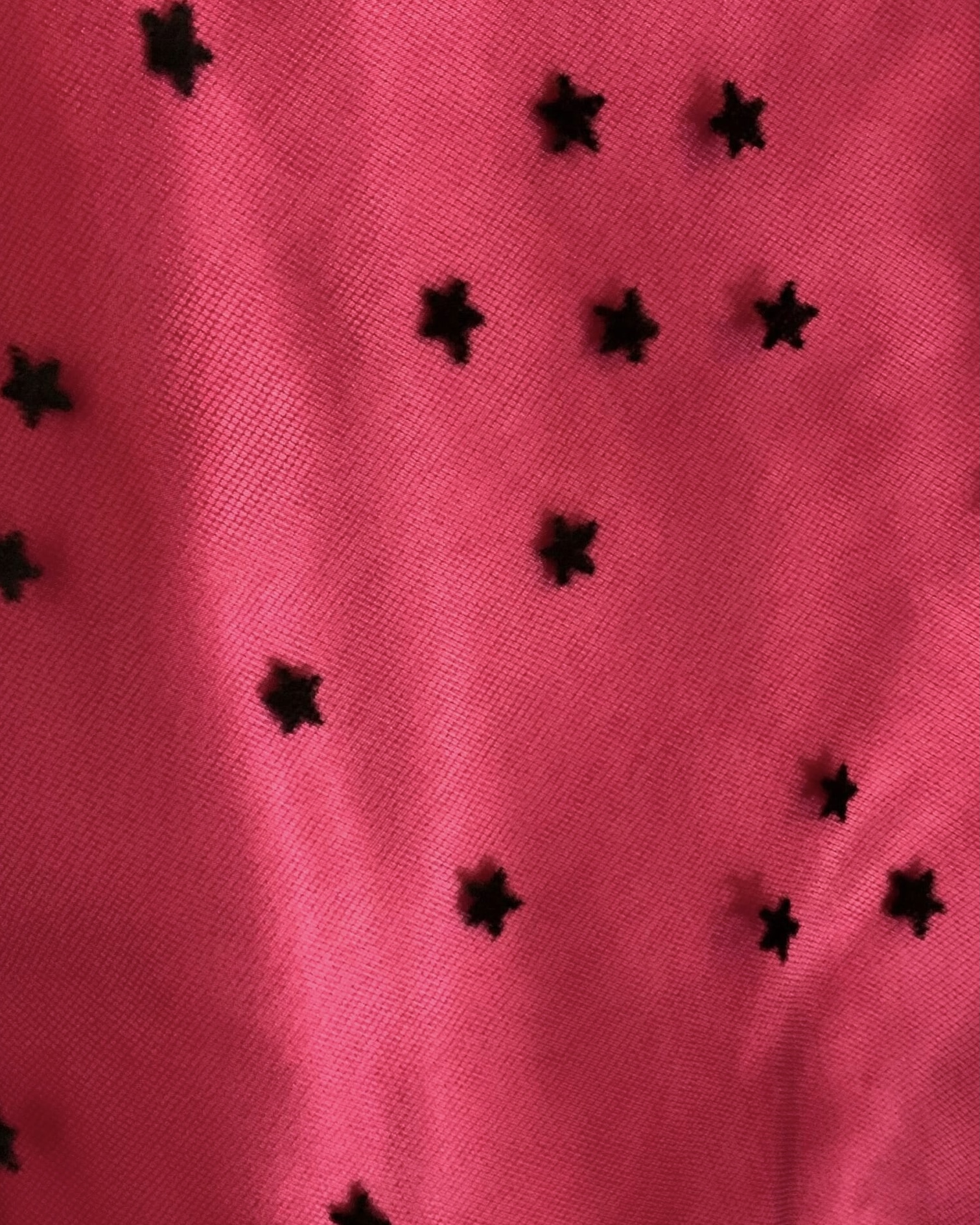 Close-up of black flocked stars on sheer tulle over bright pink gown fabric.