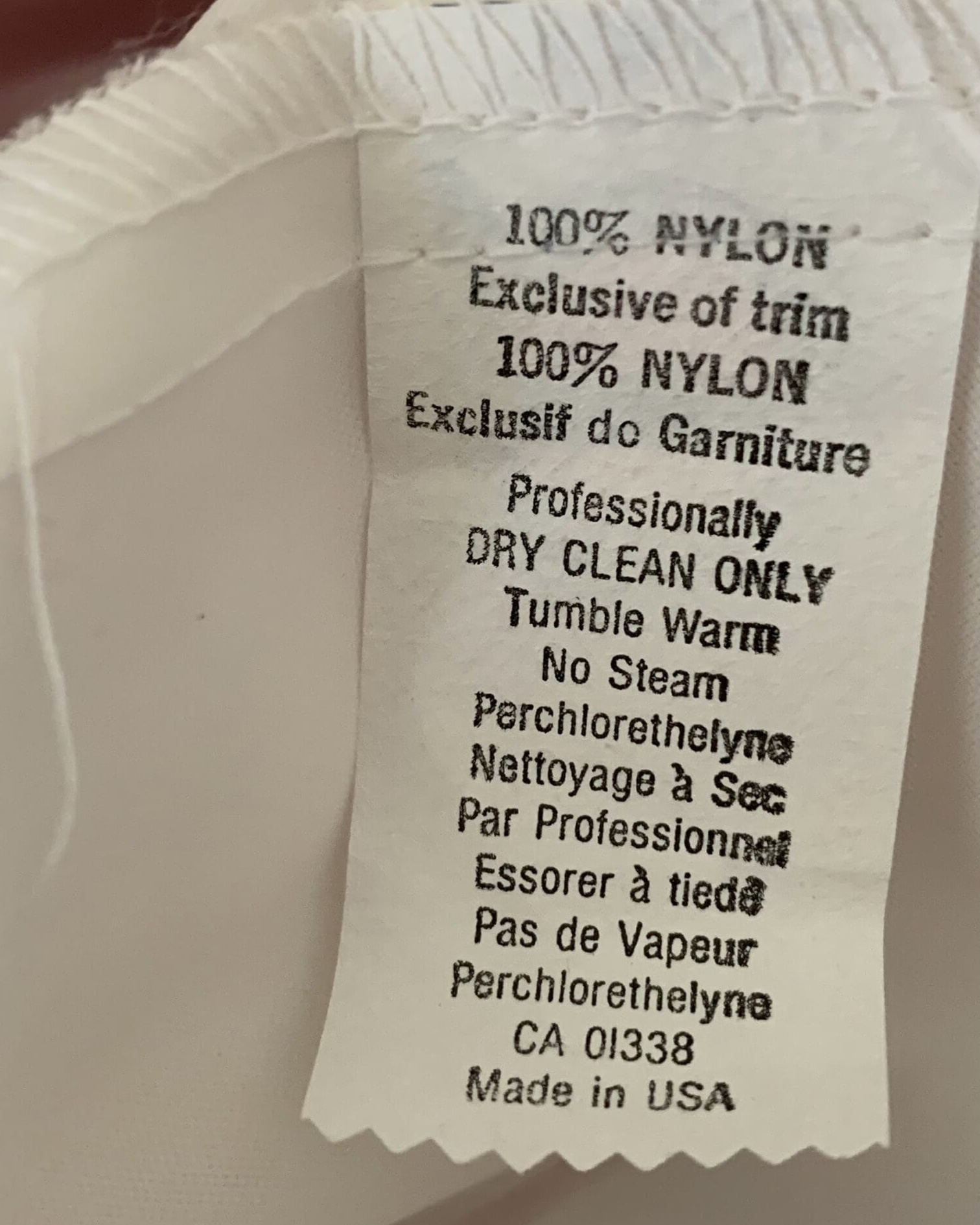 Gown care label stating 100 percent nylon, exclusive of trim, professionally dry clean only, and made in USA.