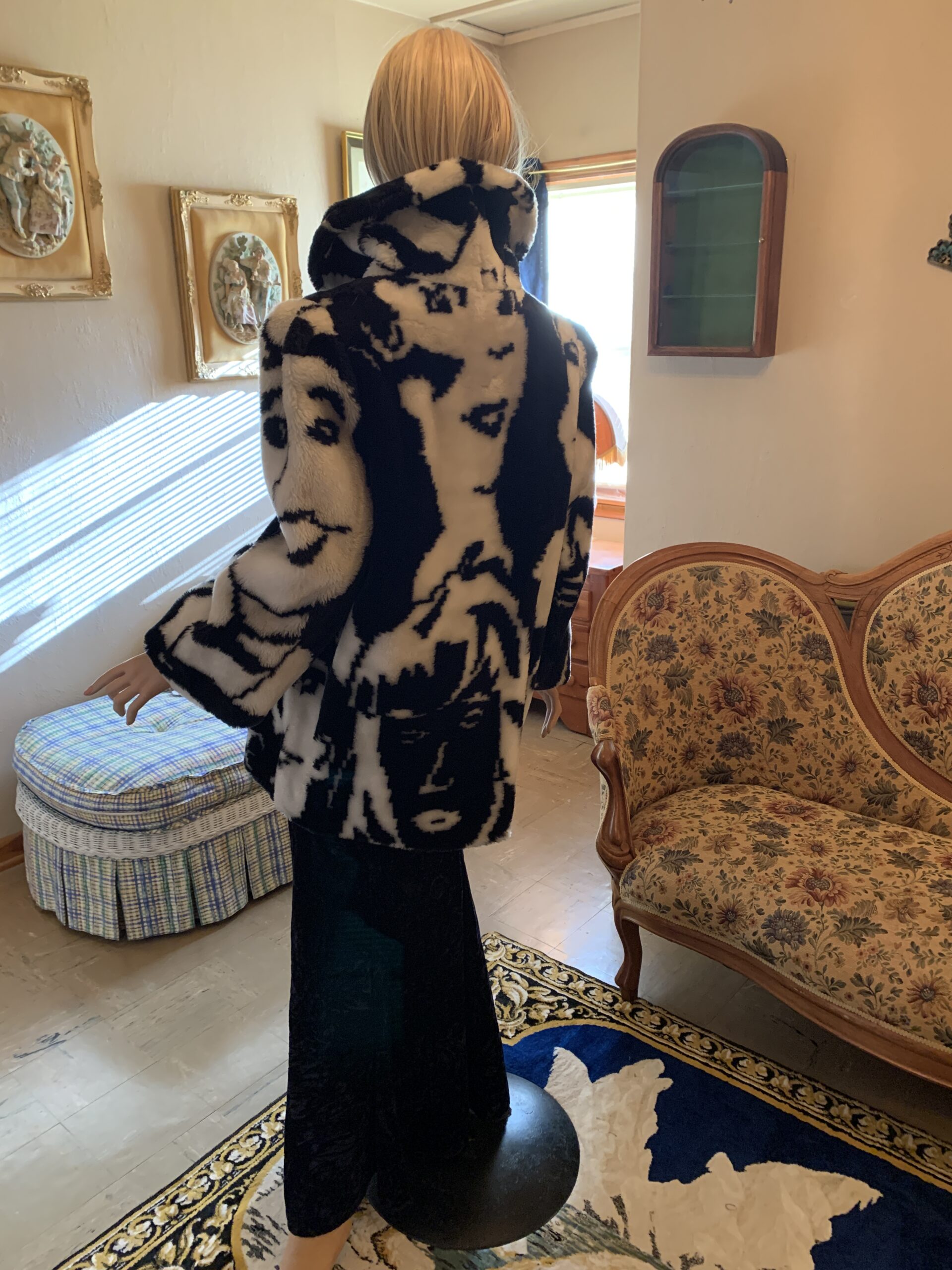 Back view of vintage black and white faux fur coat displaying bold graphic portrait motifs across the shoulders and body.