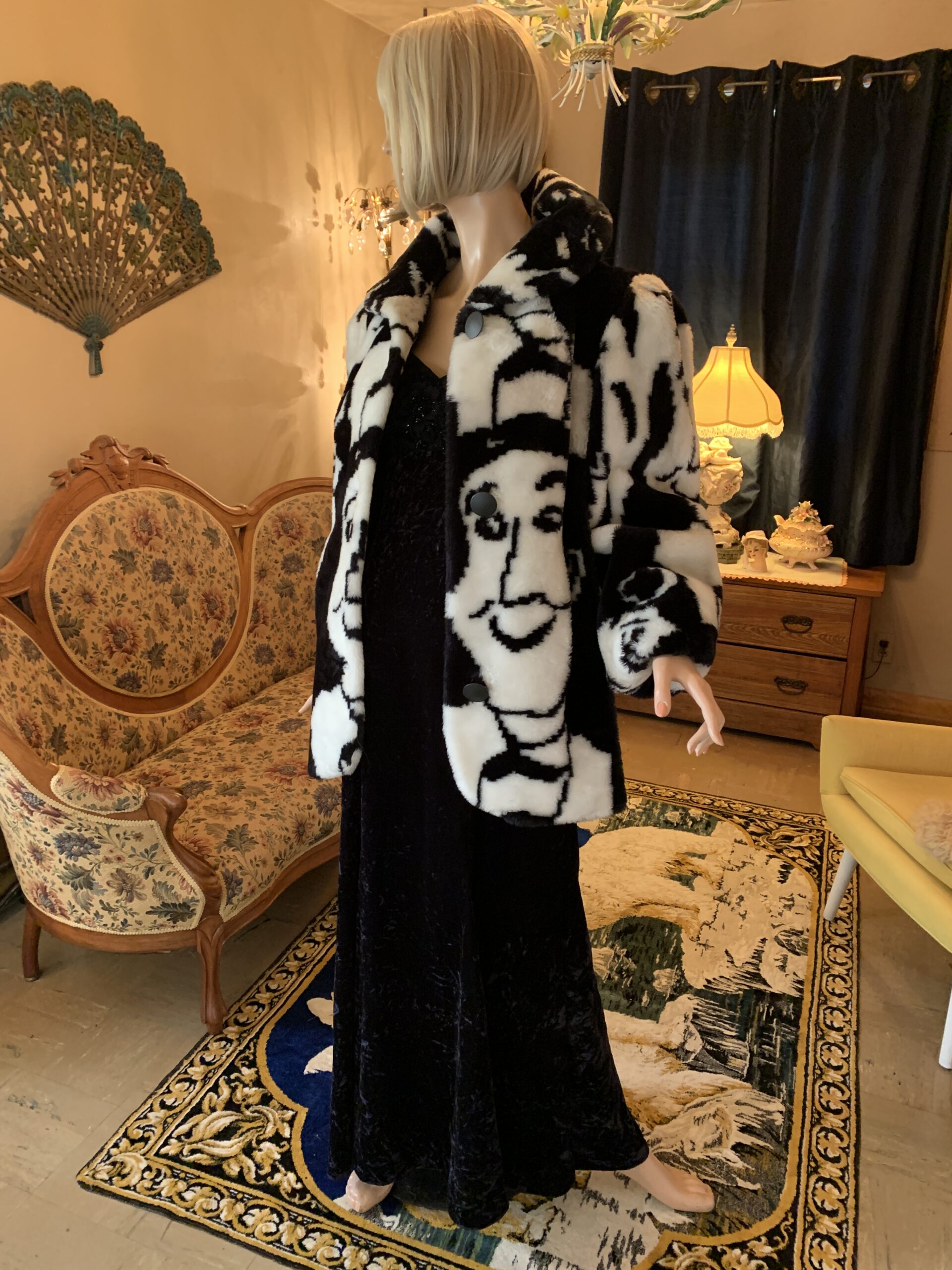 Abstract face print faux fur coat with large collar and button front closure, shown partially open over a black velvet dress.