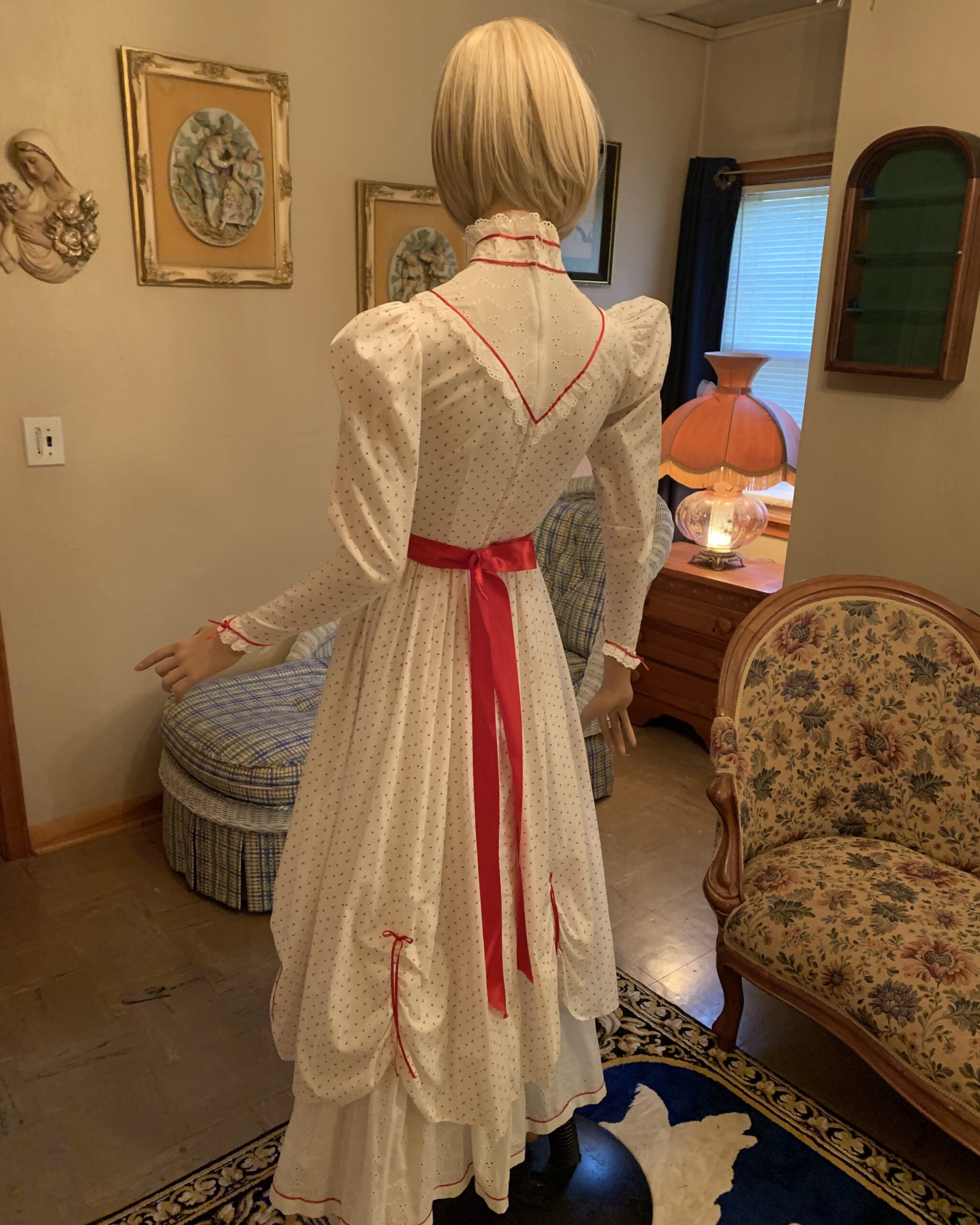 Back view of a handmade vintage prairie dress featuring a red ribbon waist tie, eyelet trim, and heart print fabric.