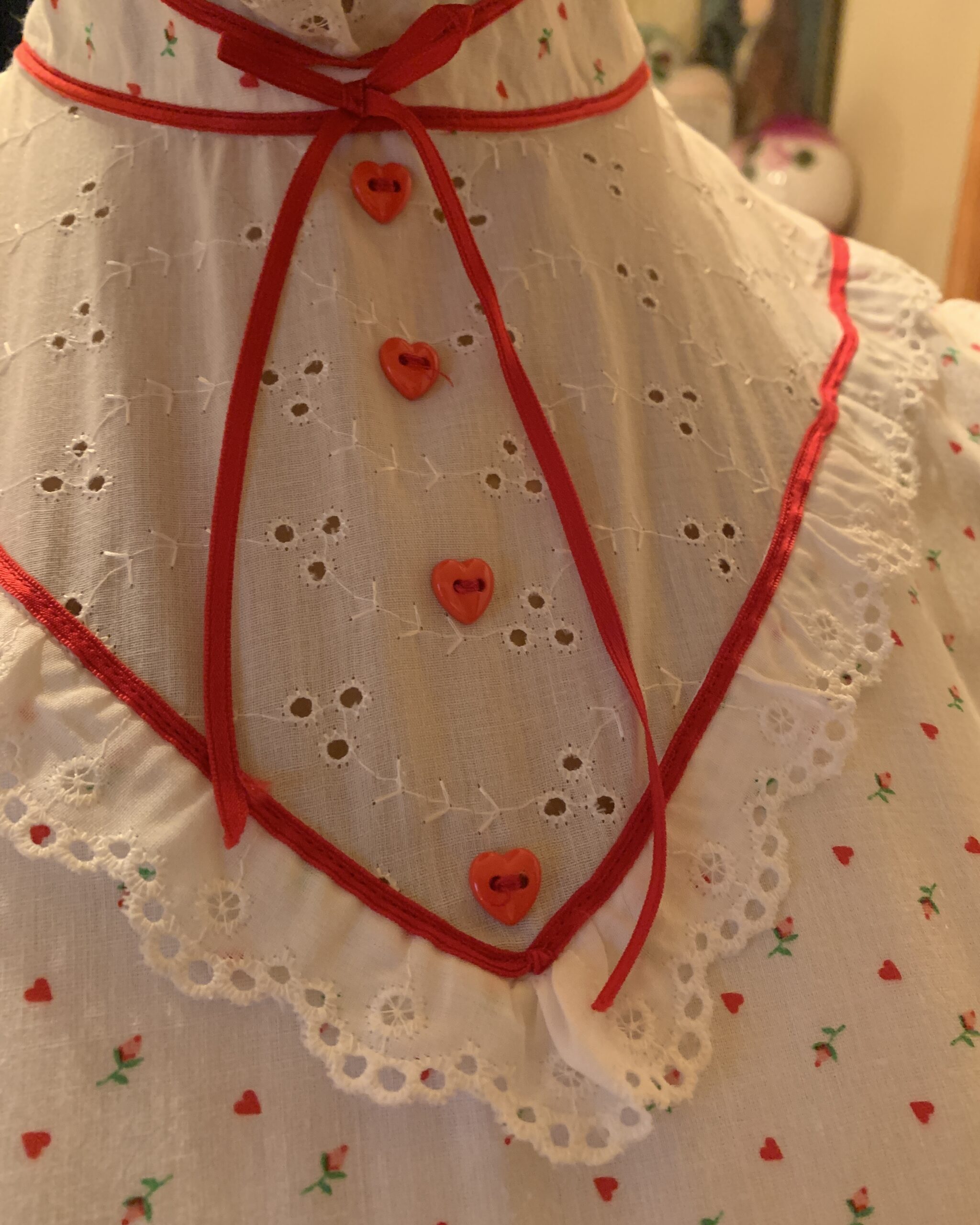 Close-up of the dress’s eyelet lace yoke with red piping, ribbon tie, and heart-shaped buttons.