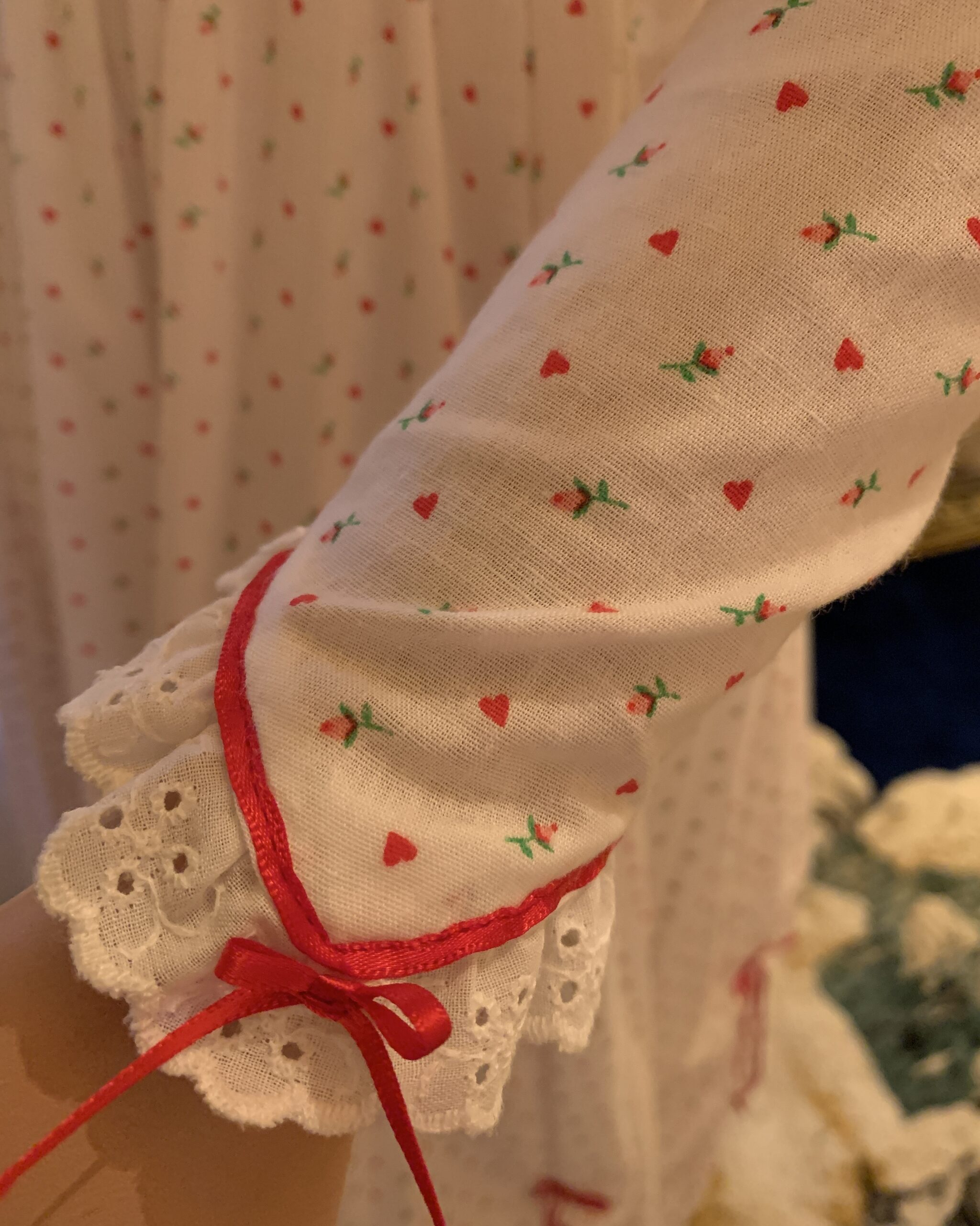 Close-up of the prairie dress sleeve showing miniature heart print fabric, eyelet lace cuff, red piping, and ribbon bow detail.