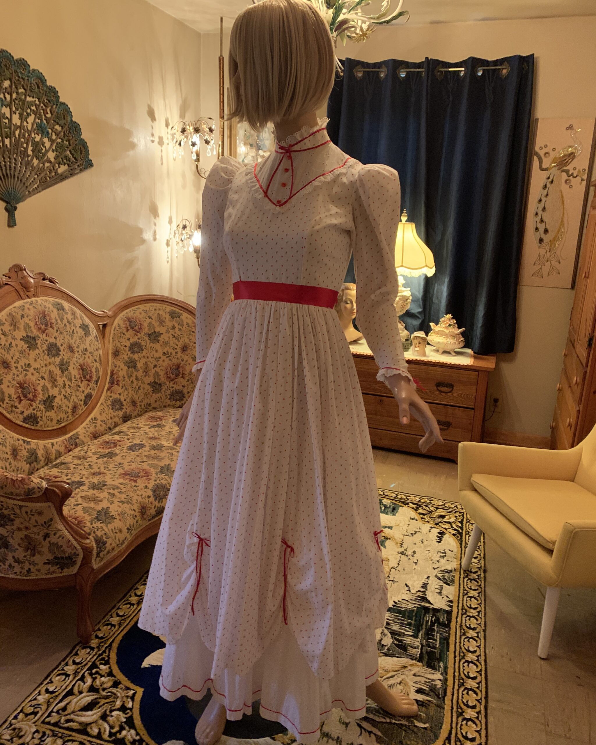 Three-quarter view of a handmade vintage prairie dress with puff sleeves, heart print fabric, red trim, and gathered skirt details.