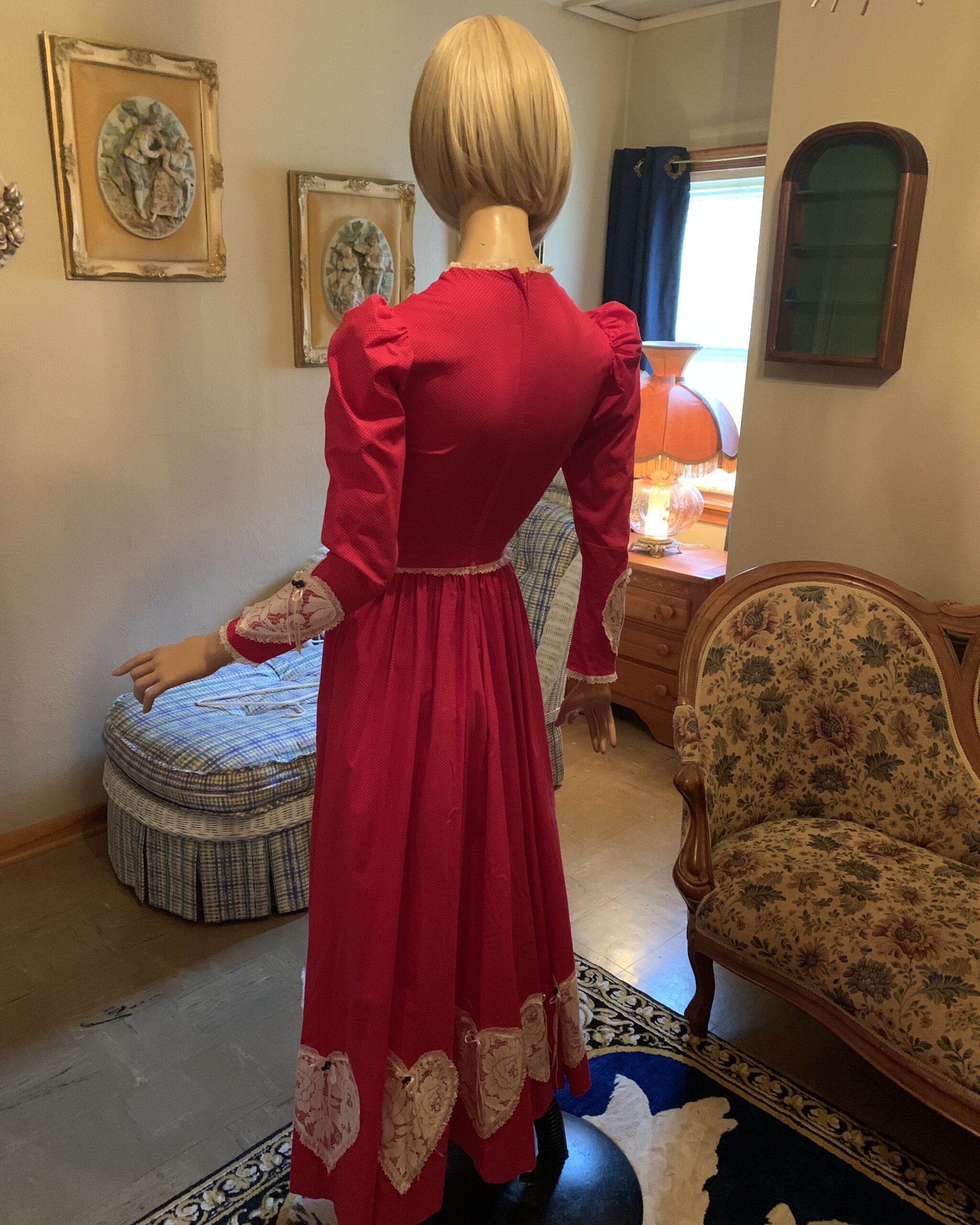 Back view of vintage handmade red prairie dress featuring fitted bodice, gathered skirt, and lace-trimmed hem appliqués.
