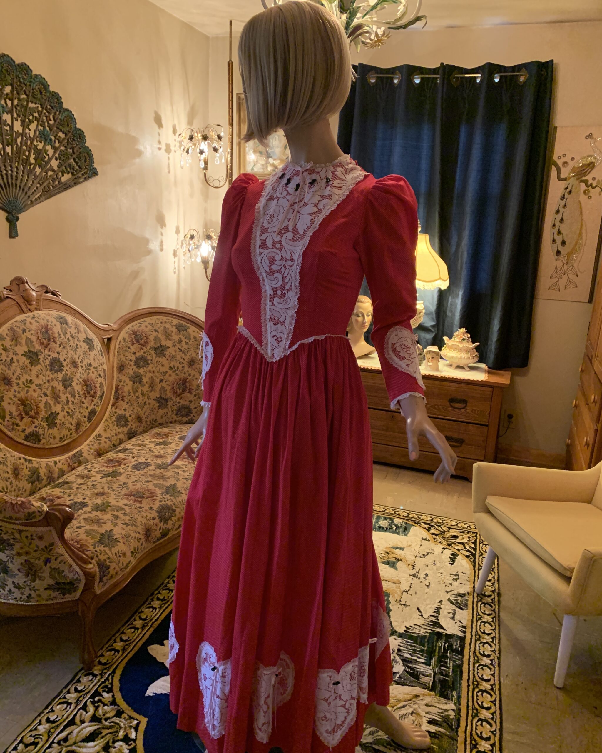 Vintage handmade red prairie dress with white lace bib, puff sleeves, musical note buttons, and gathered skirt displayed on mannequin.