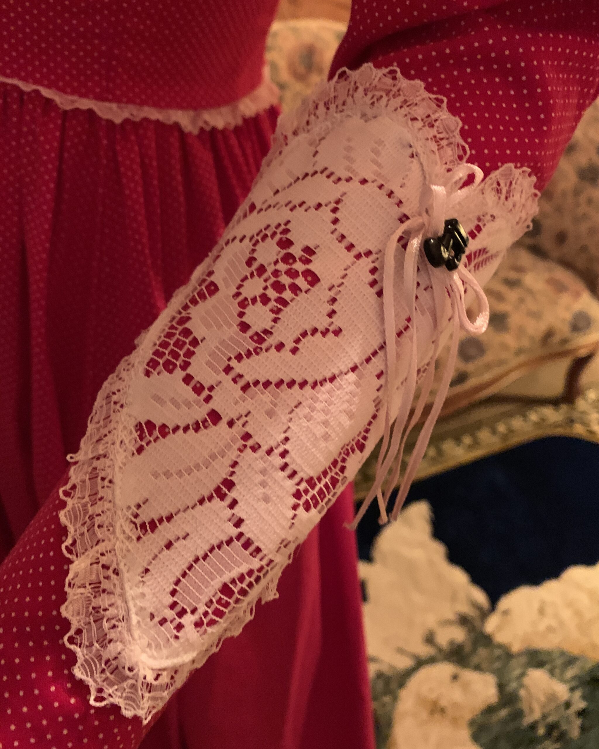 Close-up of white lace cuff appliqué with ribbon tie detail on handmade red polka dot prairie dress.