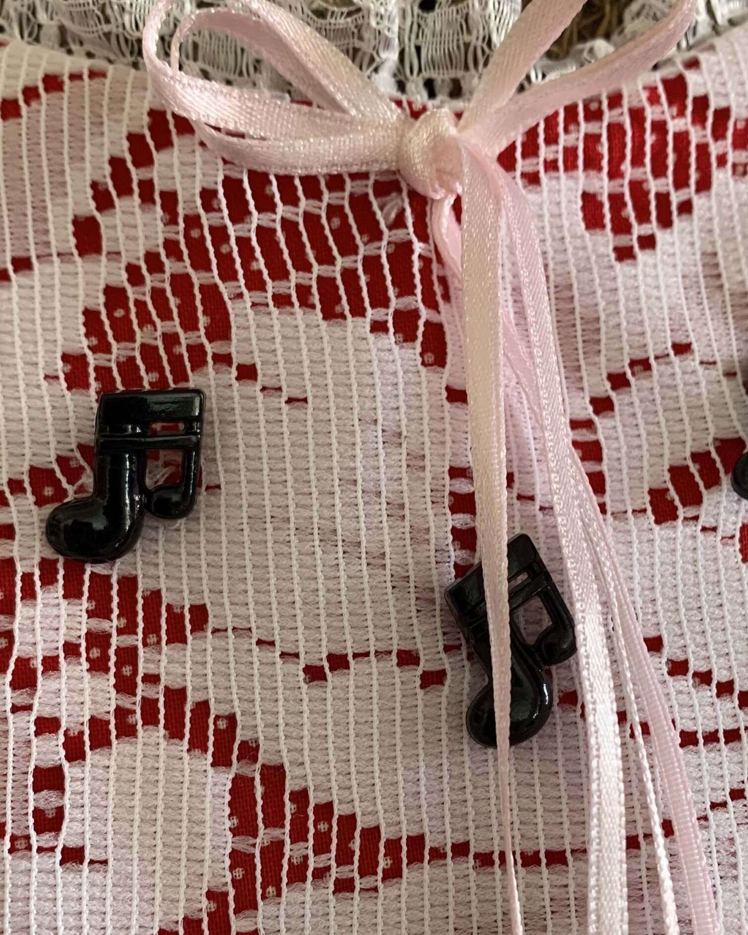 Close-up of black musical note buttons and lace-trimmed bib detail on vintage handmade red prairie dress.
