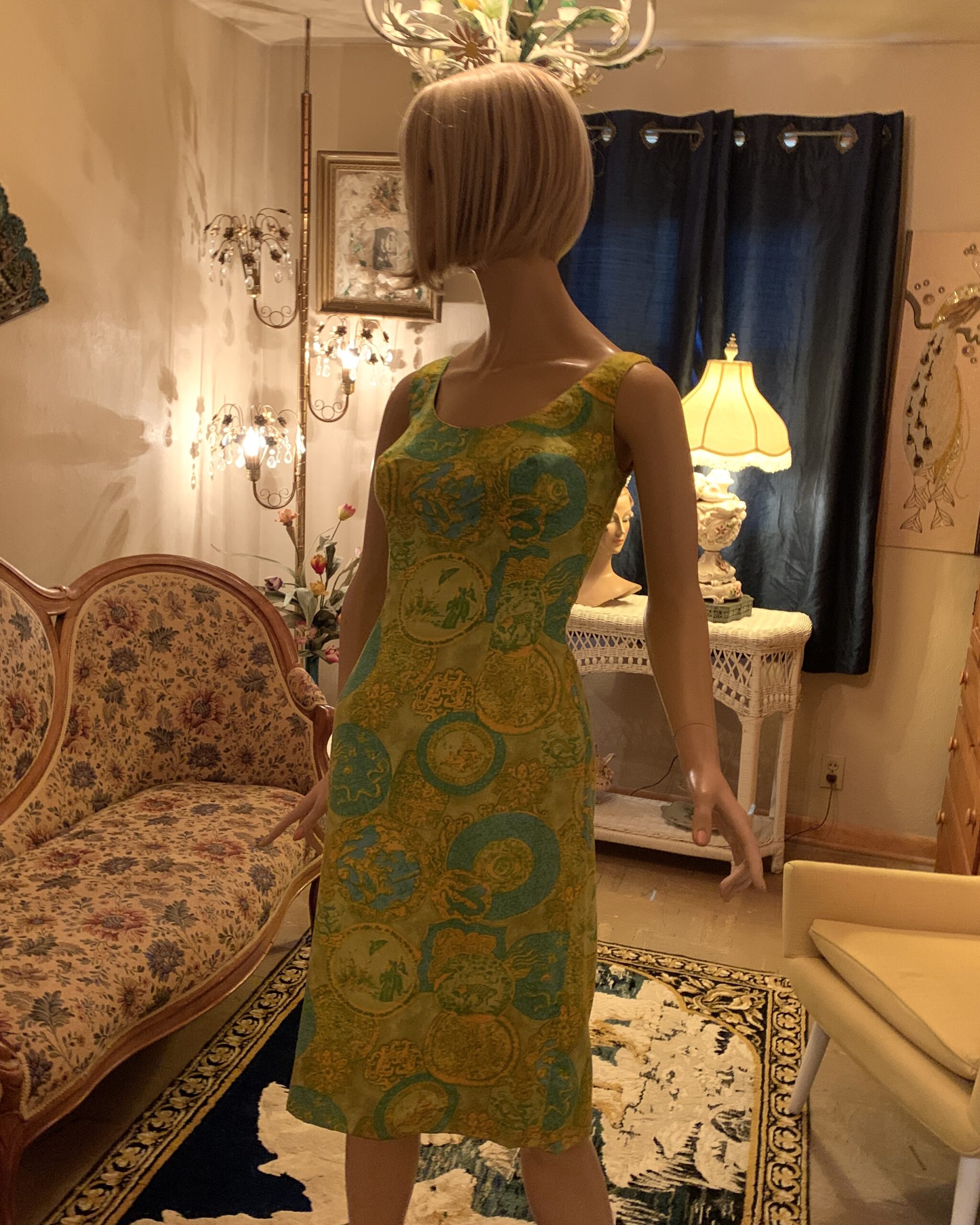 Angled front view of a late 1970s Dynasty novelty print dress in chartreuse and turquoise with fitted bodice and straight skirt, displayed on a mannequin.