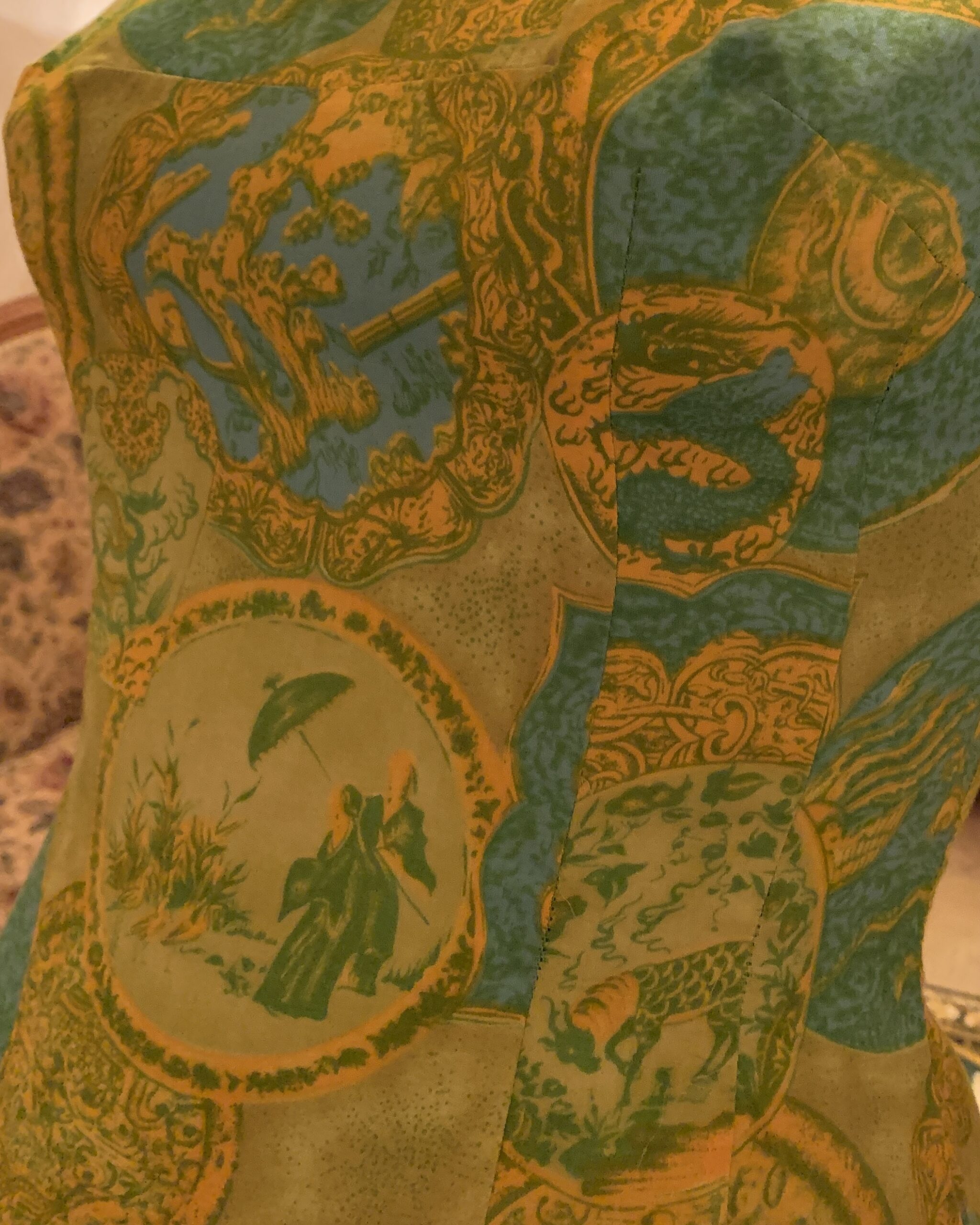 Close-up of the Dynasty dress’s novelty print featuring illustrated scenic medallions, botanical motifs, birds, and decorative ornamental designs in chartreuse, turquoise, and gold.
