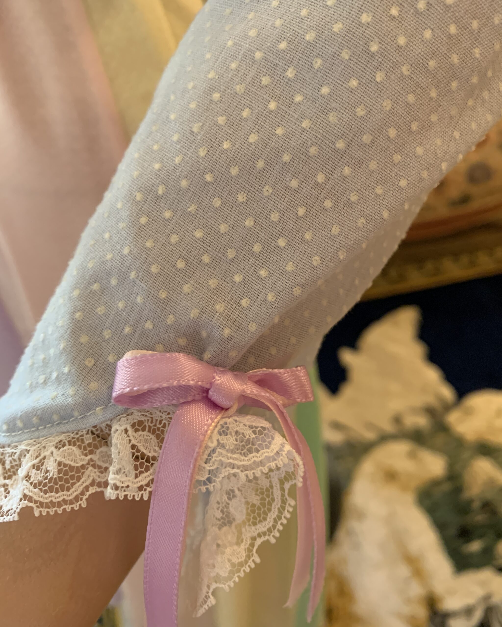Close-up of the lace-trimmed cuff with pink ribbon bow on a handmade pastel prairie dress.