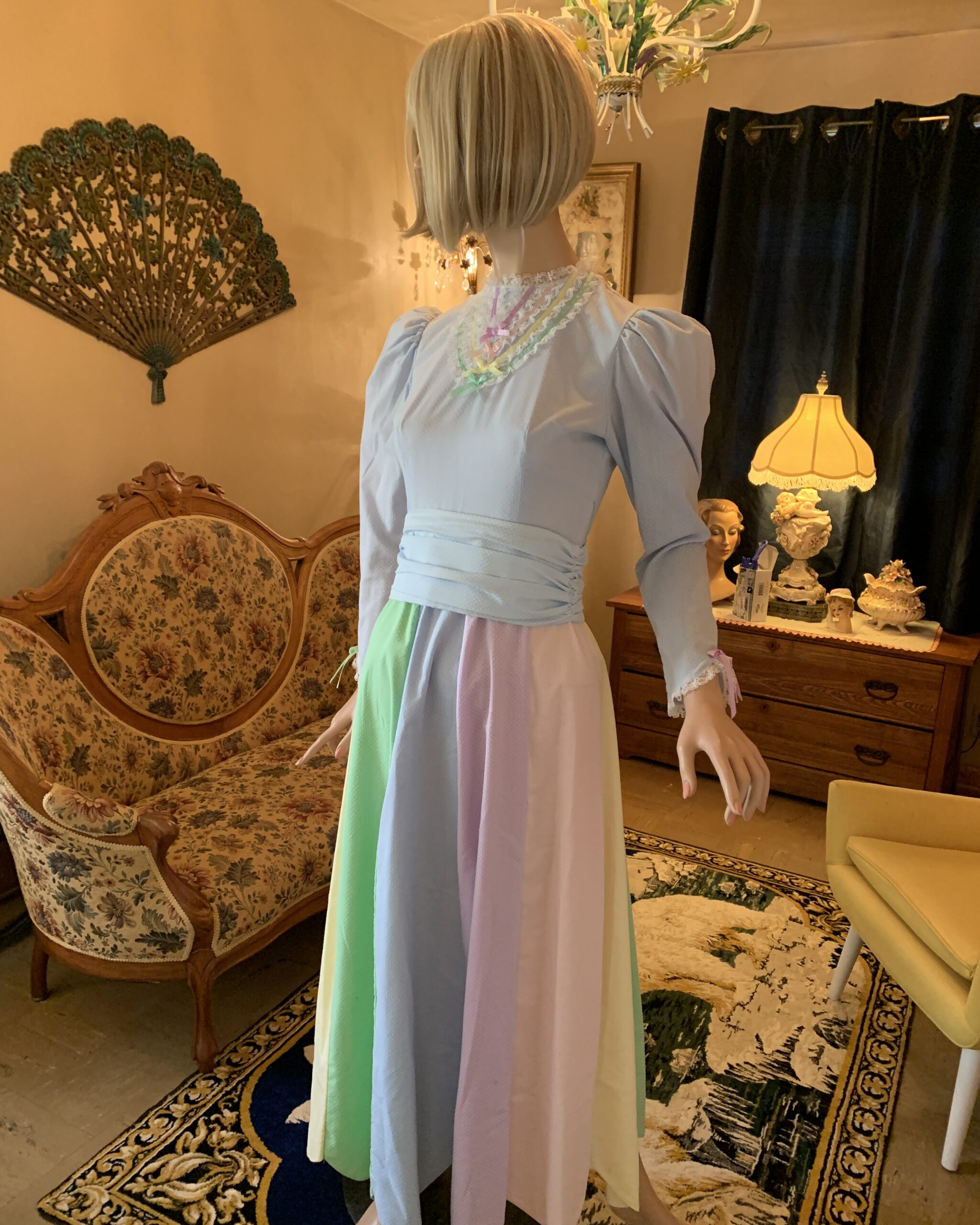 Handmade pastel prairie dress with puff sleeves, lace trim, ribbon details, and a pastel panel skirt displayed in the salon.