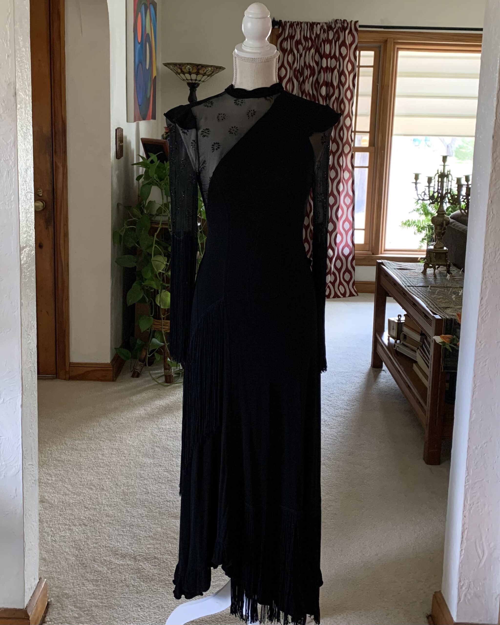1970s black fringe evening gown with sheer beaded mesh sleeves and asymmetrical draped silhouette photographed in an architectural interior setting