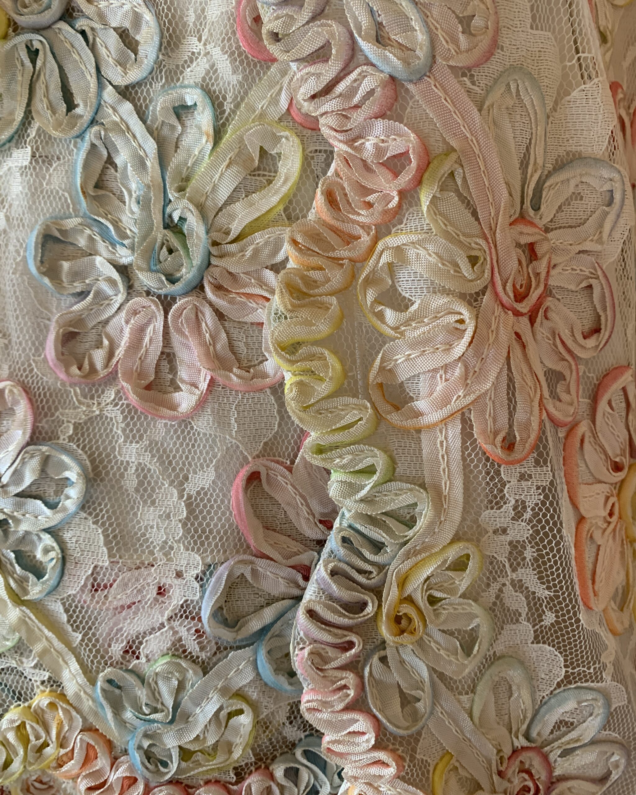 Detailed view of pastel dimensional ribbonwork floral appliqué on vintage lace dress with multicolor ribbon embroidery.