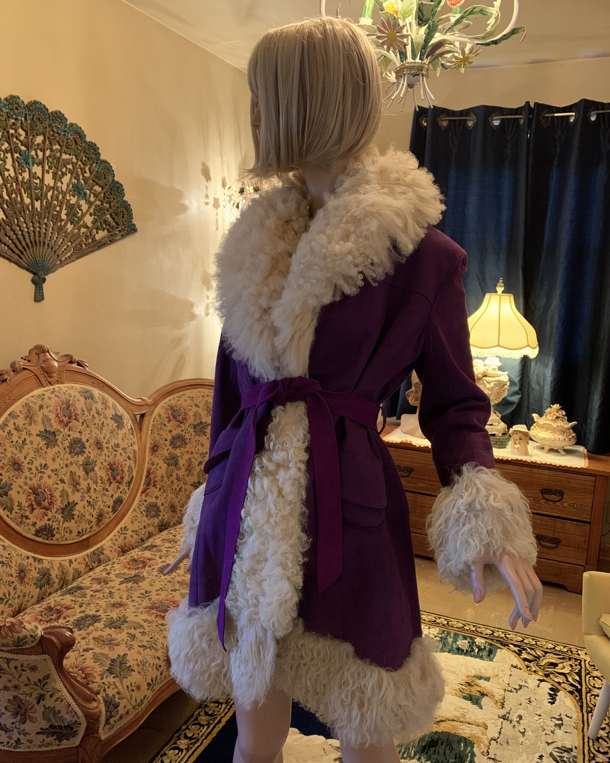 Side view of a vintage Lilli Ann purple coat with cream curly shearling trim, self-tie belt, patch pockets, and Made in England label, photographed in the salon.