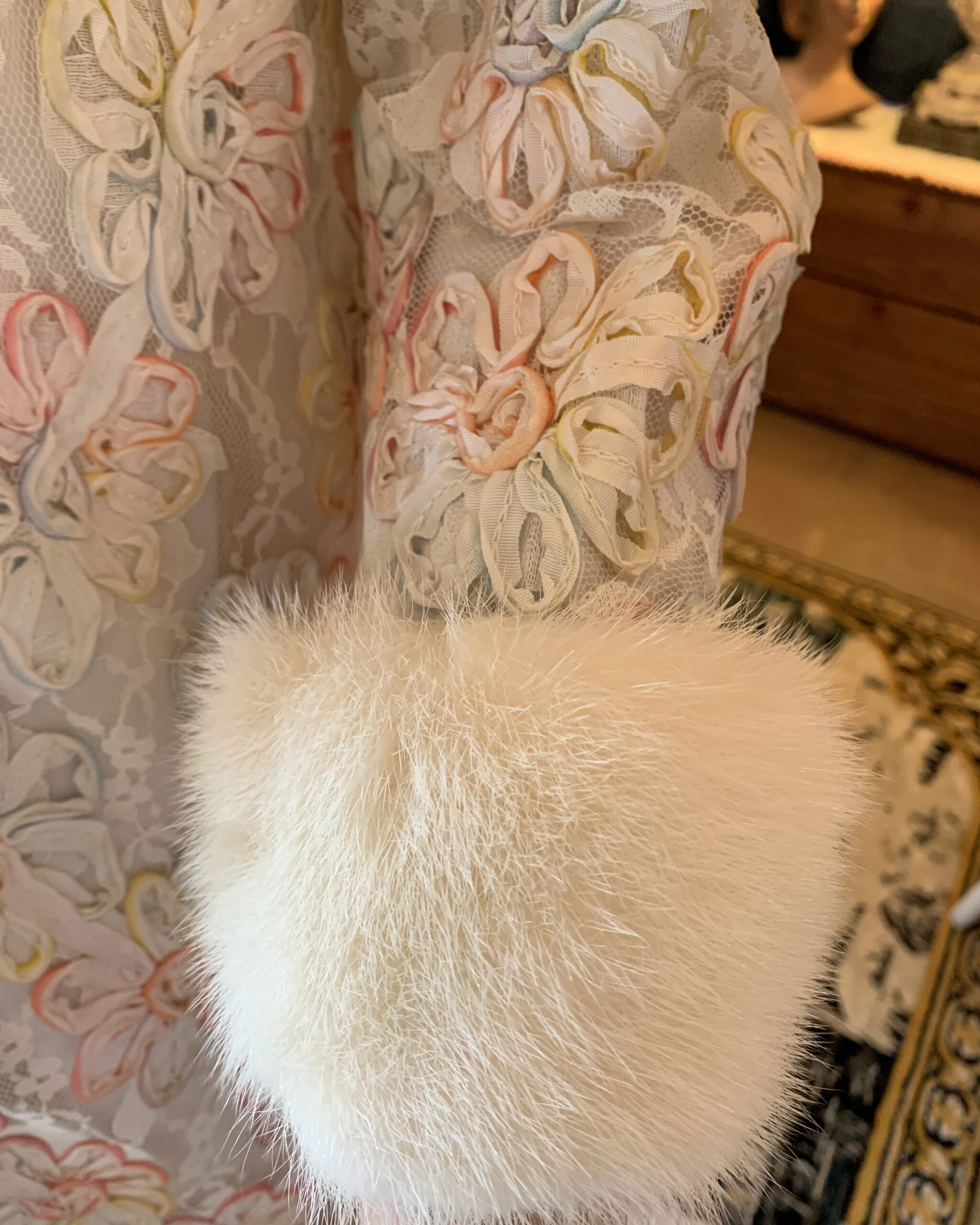 Close-up of white mink fur cuff on vintage pastel ribbonwork lace coat showing floral appliqué and lace construction.