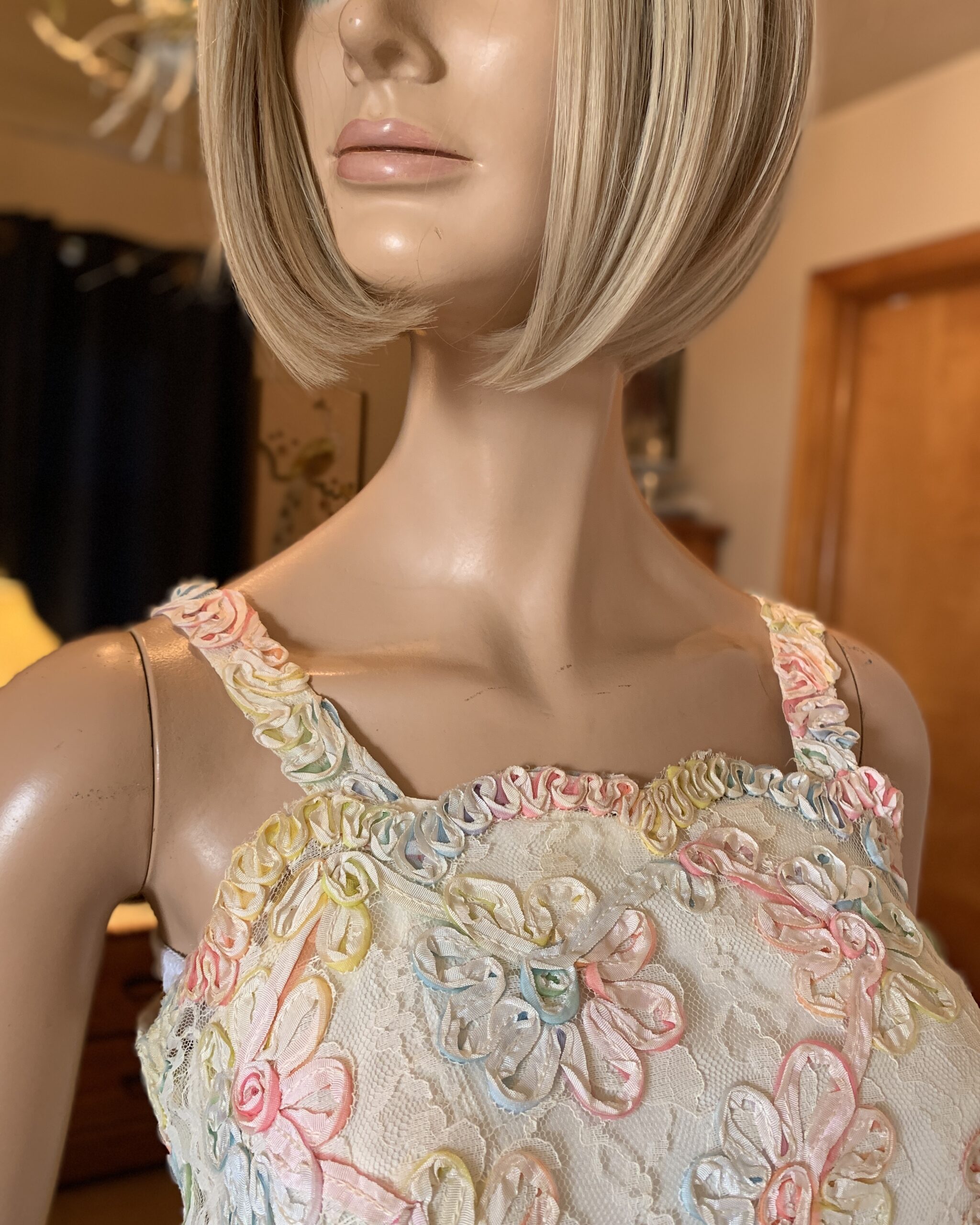Close-up of vintage pastel ribbonwork lace dress bodice showing dimensional floral ribbon appliqué and lace overlay.