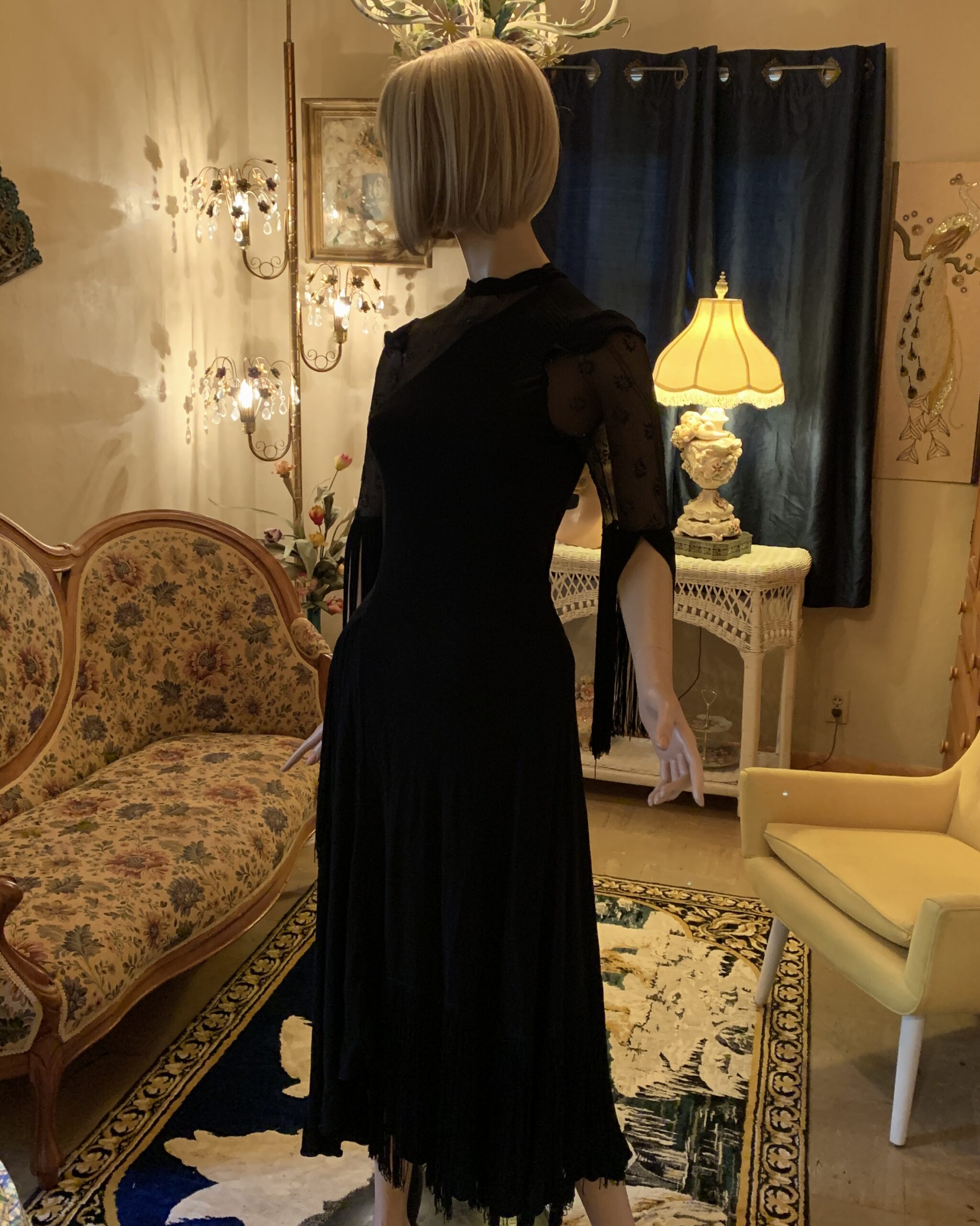 Side view of a vintage Riding High black fringe dress featuring sheer floral beaded sleeves and an asymmetrical drop-waist silhouette.