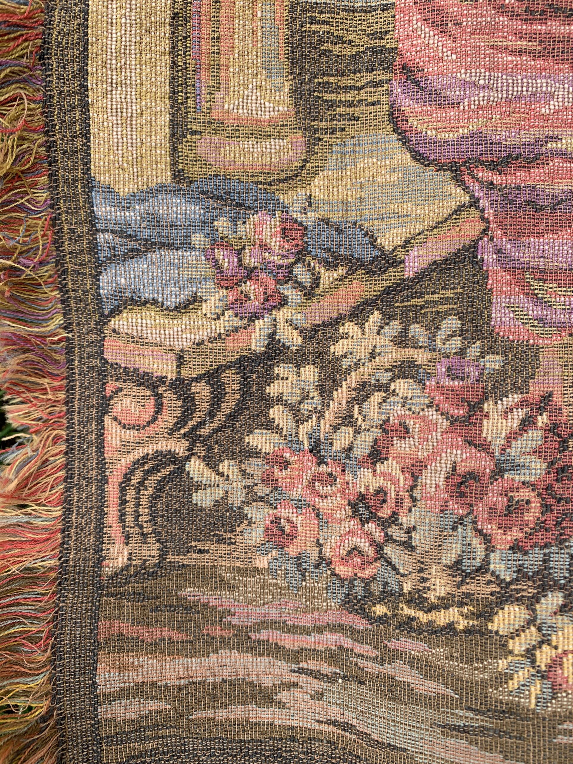 Close-up of tapestry weave, floral border, and multicolored fringe illustrating textile craftsmanship and texture.