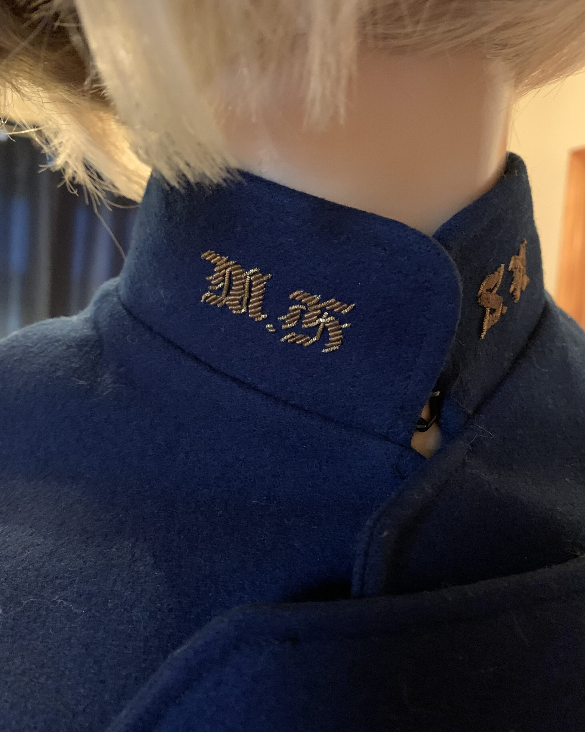 Close-up of embroidered collar detail on a vintage navy blue wool nurses cape with decorative button closures.