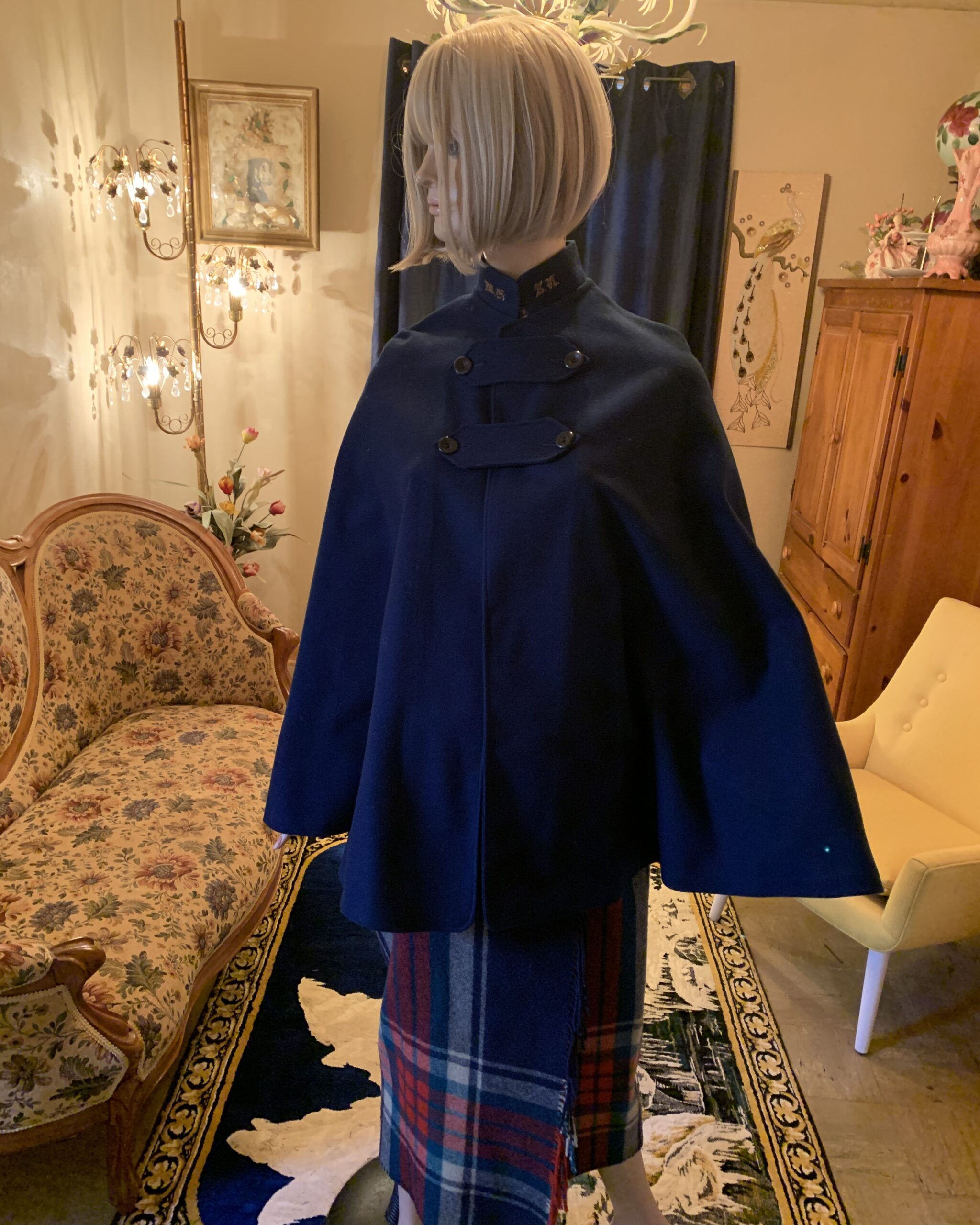 Vintage navy blue wool nurses cape with embroidered collar, military-inspired button closures, and tartan skirt styling photographed in a vintage salon interior.