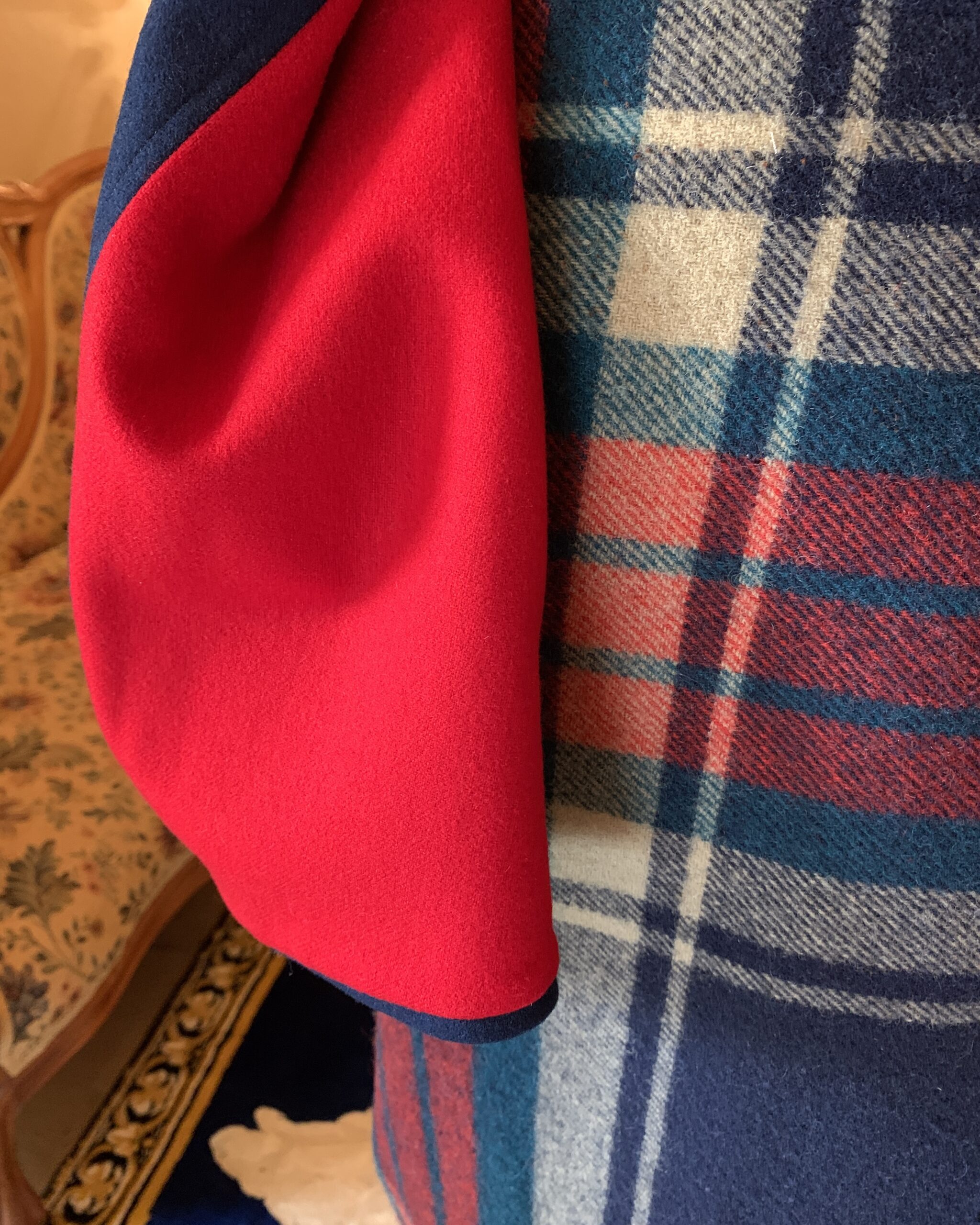 Detail of vibrant red wool lining inside a vintage navy blue nurses cape displayed against a plaid wool skirt.