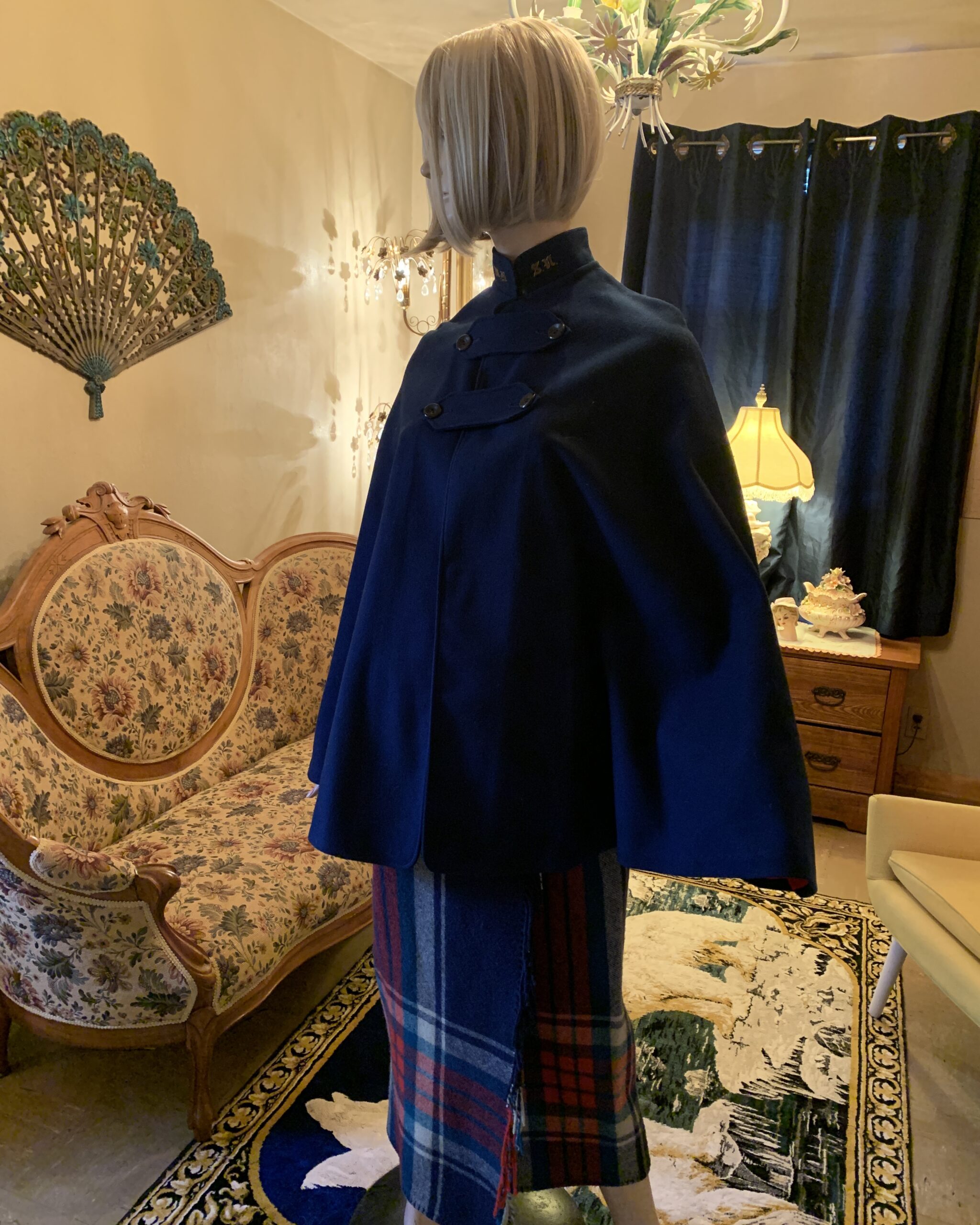 Side profile of a vintage navy wool nurses cape showing dramatic drape, embroidered standing collar, and wide cape silhouette.