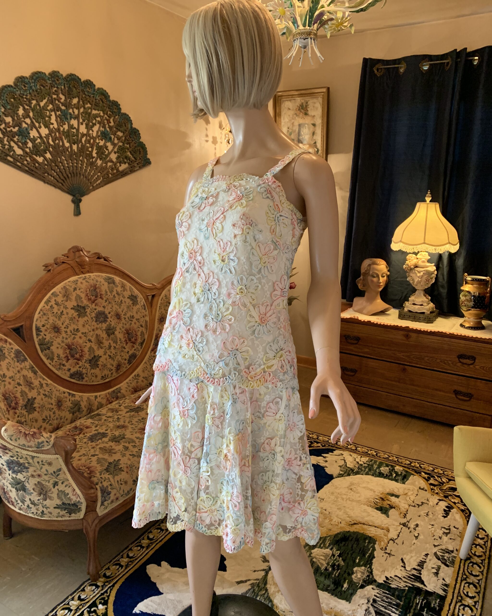 Vintage pastel ribbonwork lace cocktail dress with dimensional floral appliqué and drop waist silhouette displayed on mannequin in salon setting.