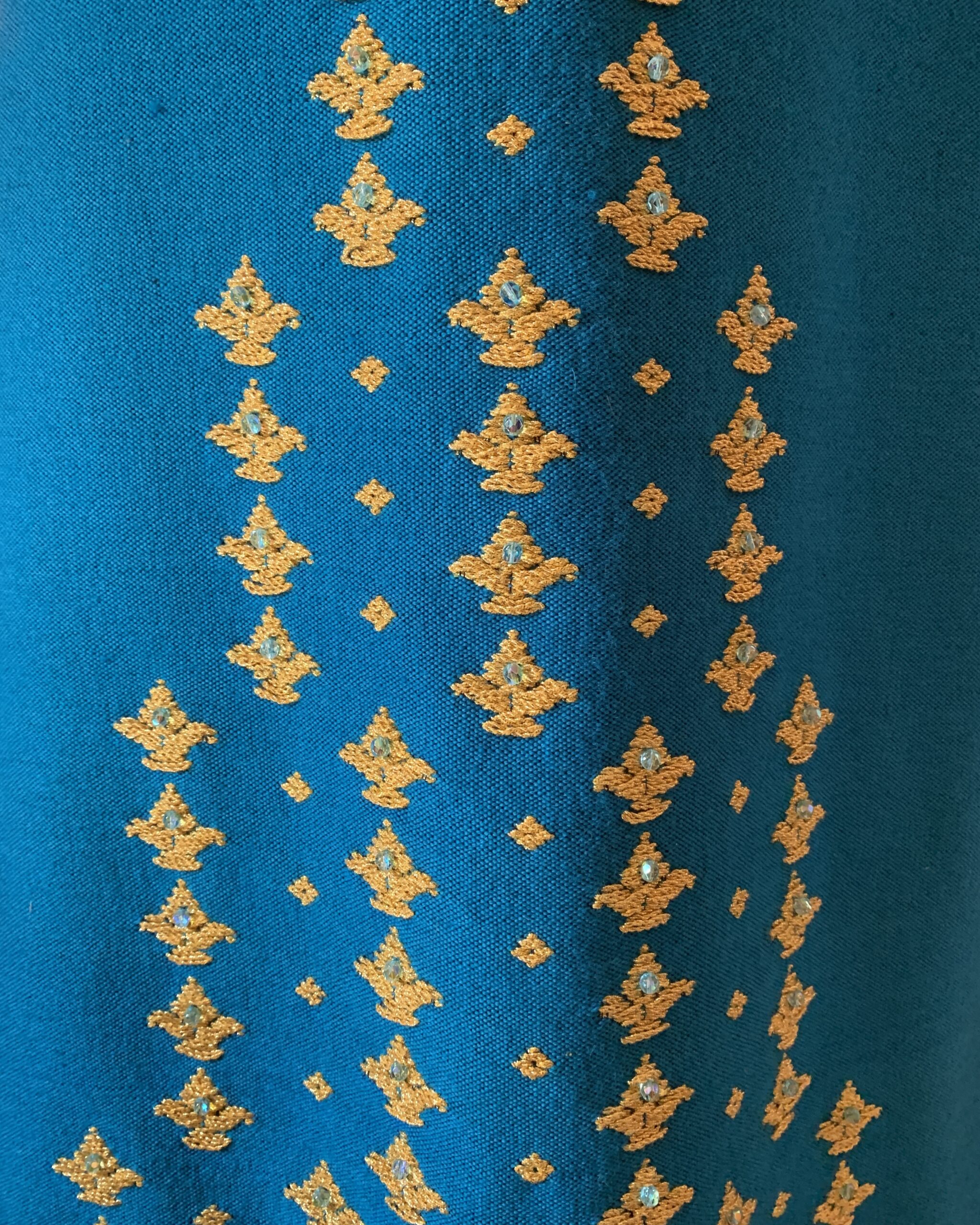 Close-up of gold metallic embroidered motifs with small reflective bead accents on blue textured fabric of 1970s Greek designer gown.