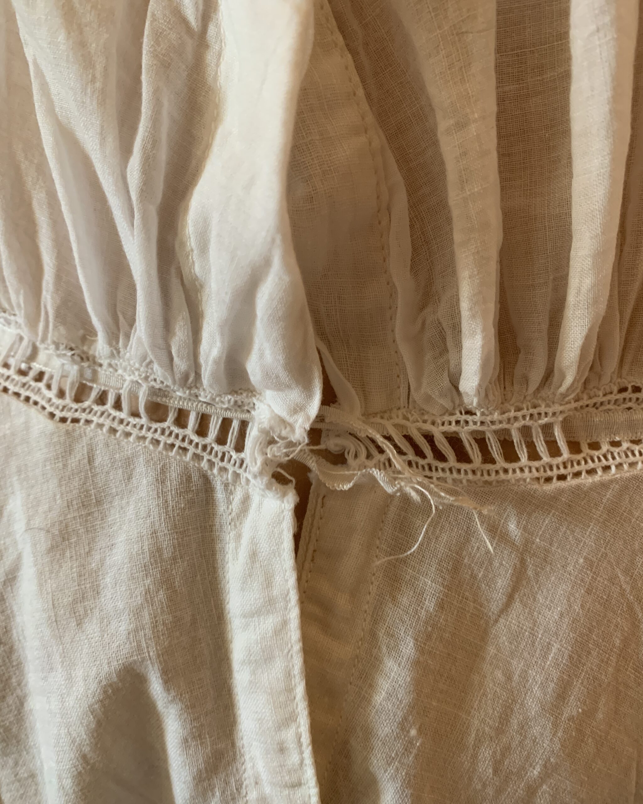 Close-up of antique Edwardian cotton combination garment showing waist insertion detail and light wear to ribbon trim.
