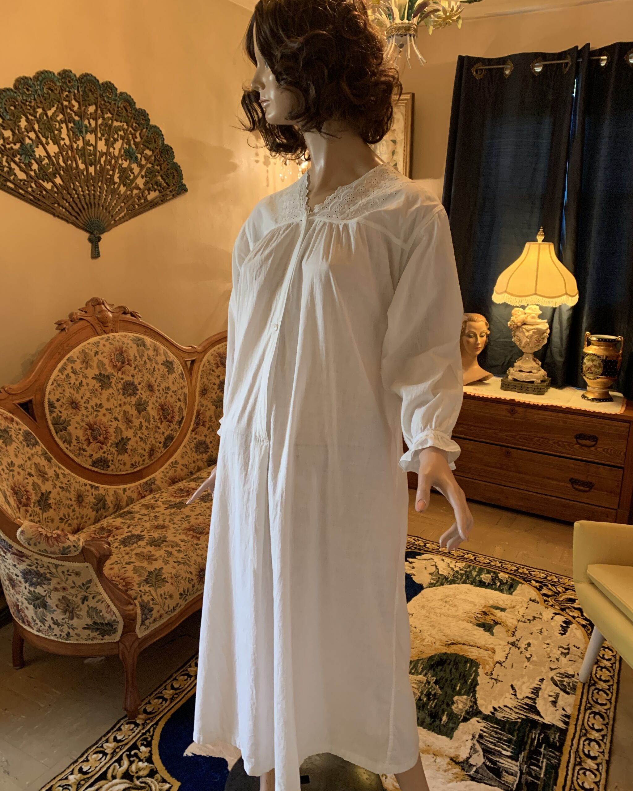 Early 20th-century white cotton nightgown displayed on mannequin featuring embroidered eyelet lace neckline, gathered bodice, long sleeves, and soft flowing silhouette.