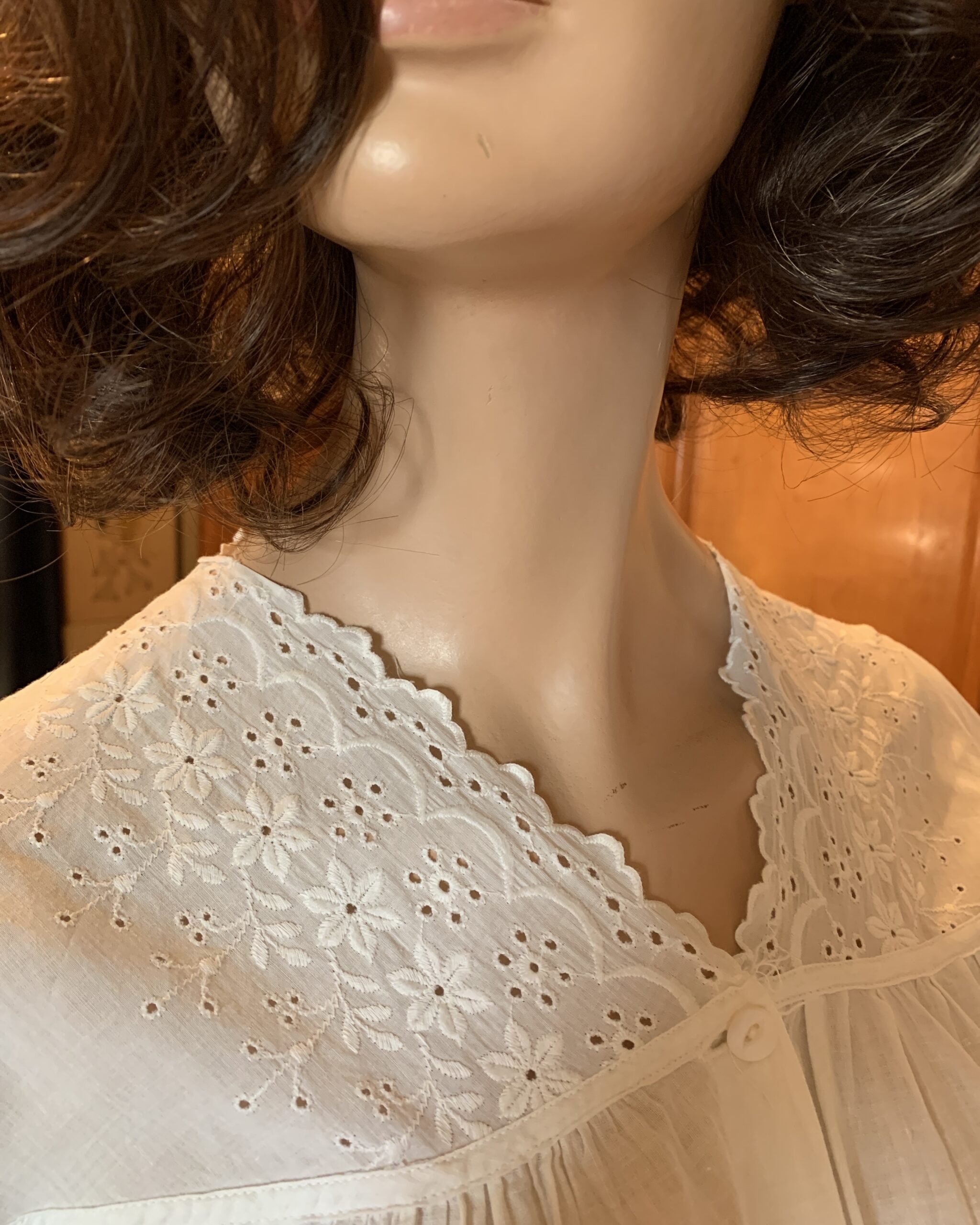 Close-up of embroidered eyelet lace collar detail on early 20th-century white cotton nightgown.