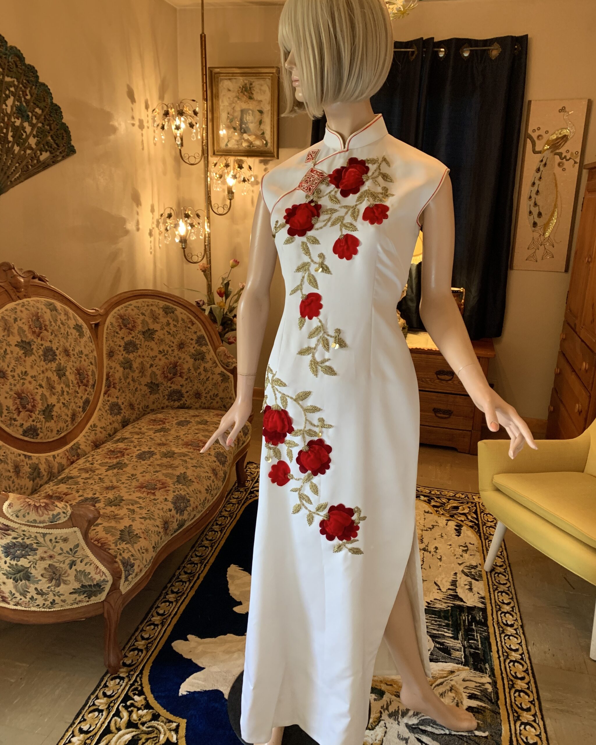Vintage ivory cheongsam dress with red velvet floral appliqué and gold beaded embroidery, sleeveless Mandarin collar gown displayed on mannequin.