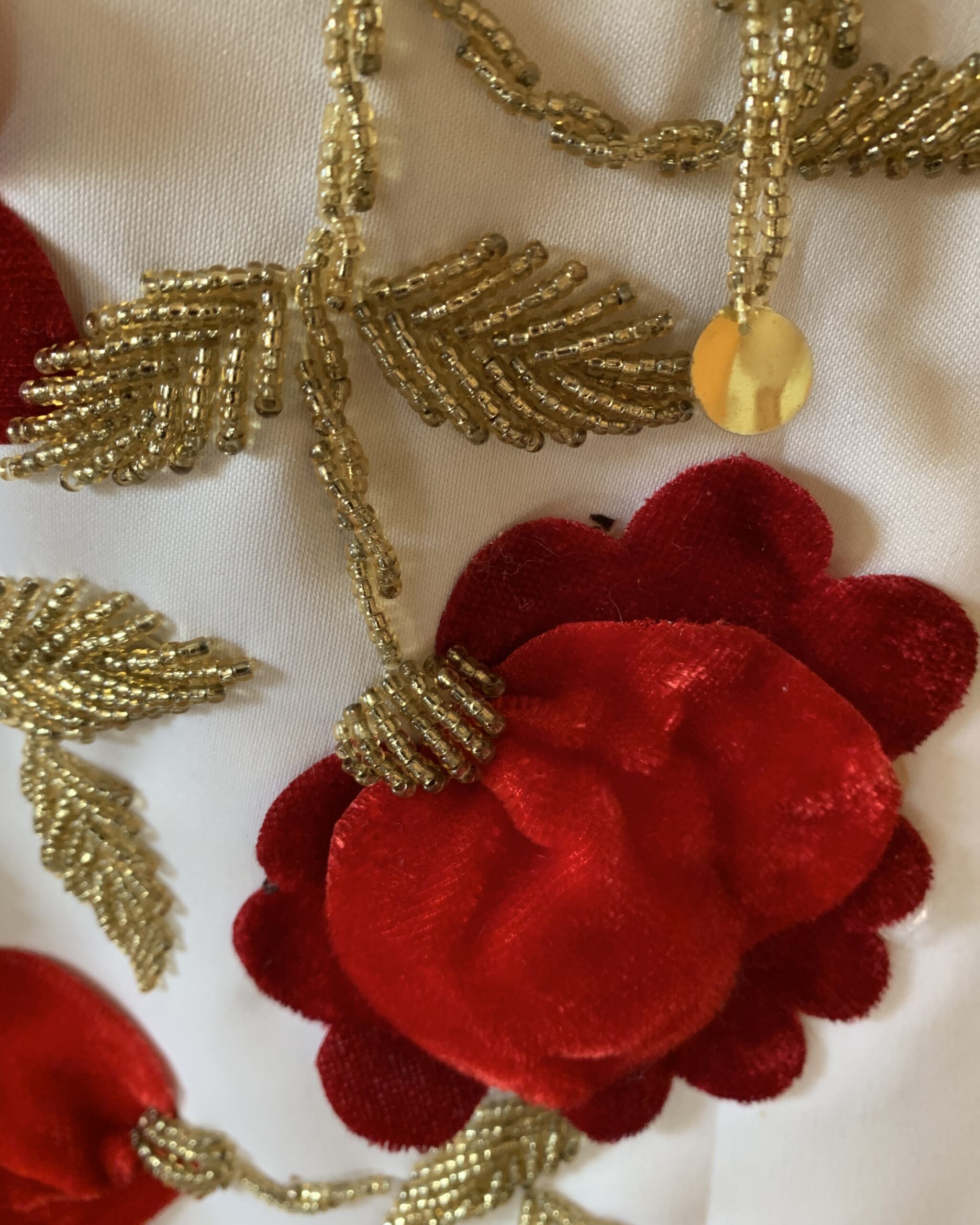 Close-up of dimensional red velvet flower appliqué with gold glass bead embroidery on vintage ivory cheongsam gown.