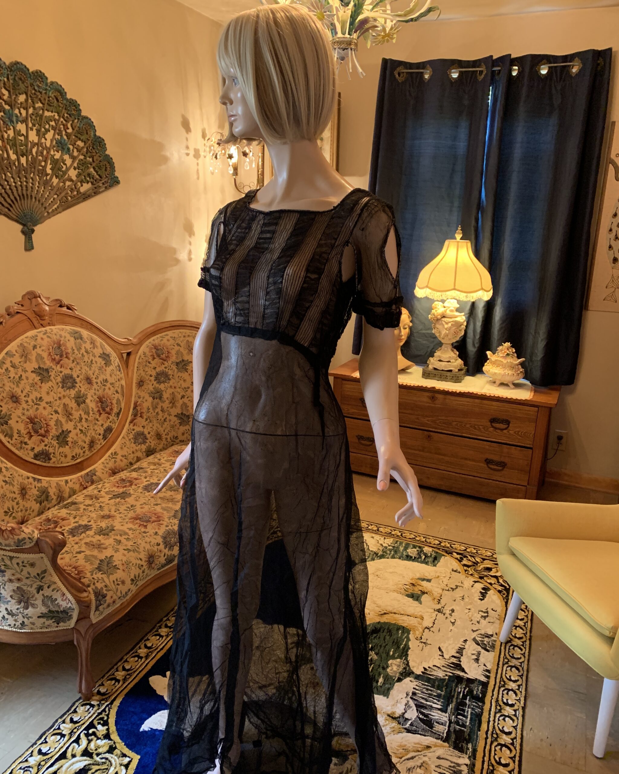 Vintage c. 1930–1933 sheer black evening gown displayed on a mannequin with vertical net detailing, beaded open shoulder sleeves, and a flowing sheer skirt.