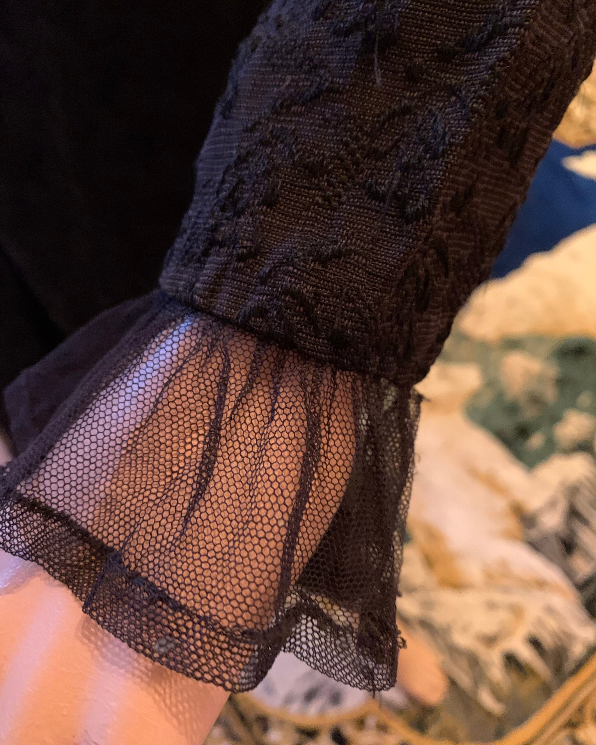Close-up of the dress sleeve showing a sheer black lace cuff with gathered trim and floral woven fabric.