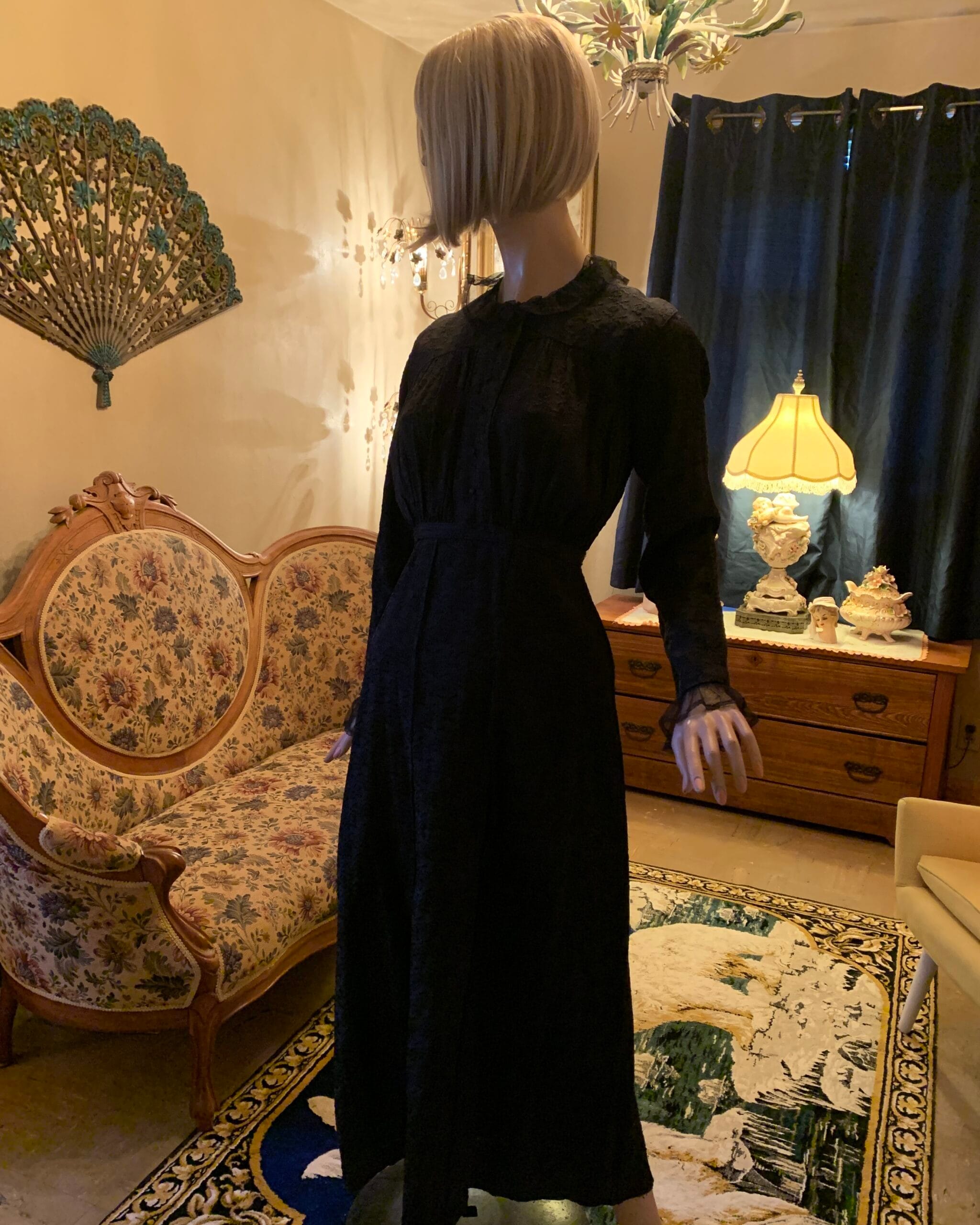Antique black floral woven dress with ruffled neckline and lace cuffs photographed in warm lamplight inside a vintage salon.