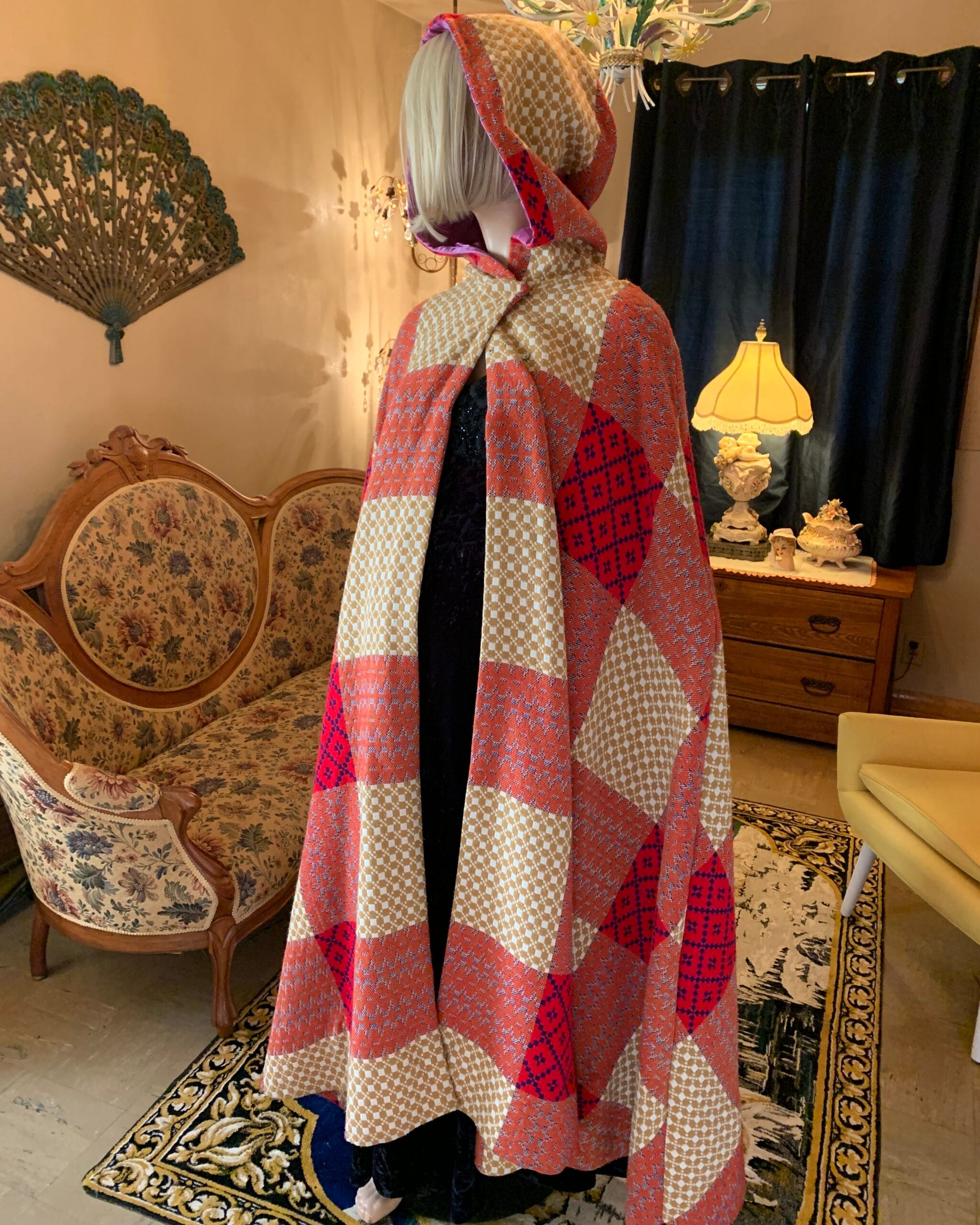 Angled view of a hooded patchwork tapestry cape with raised hood and dramatic full silhouette.