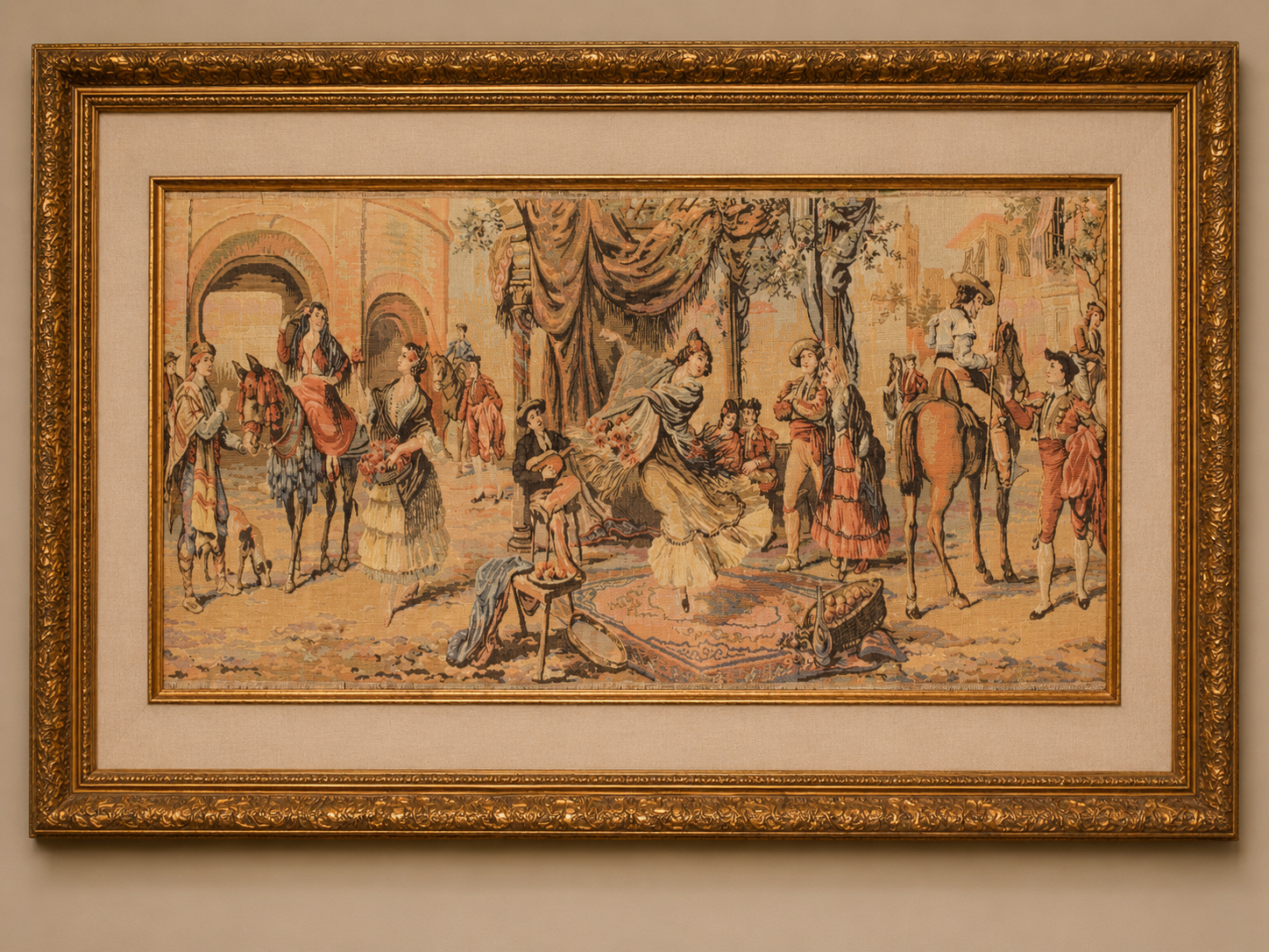 Framed visualization of a vintage tapestry depicting a lively Spanish courtyard scene with dancers, horse riders, musicians, and figures gathered beneath draped fabric, presented in an ornate gold frame with linen matting.