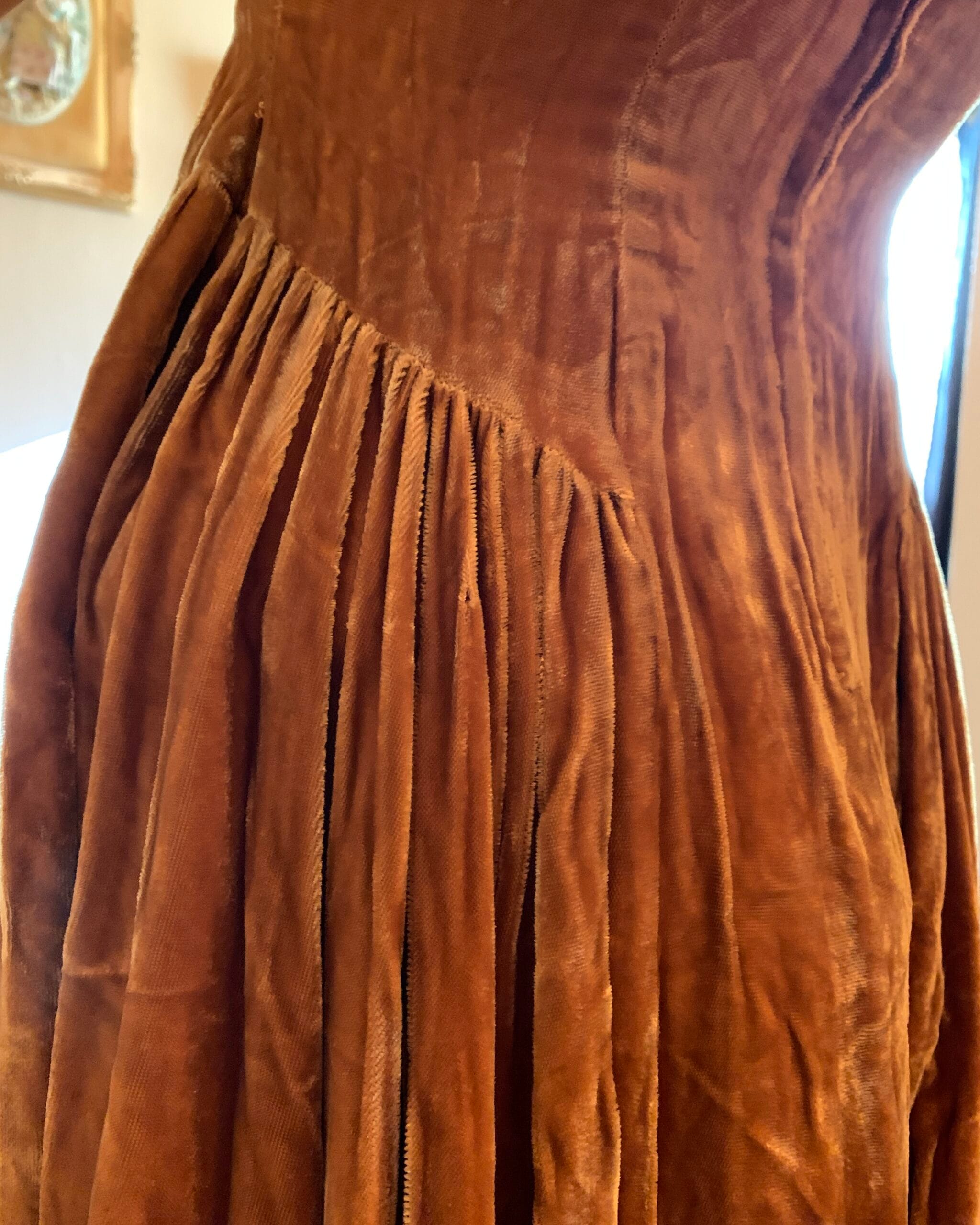 Close-up of the gathered waist and full skirt construction on a vintage golden velvet dress.
